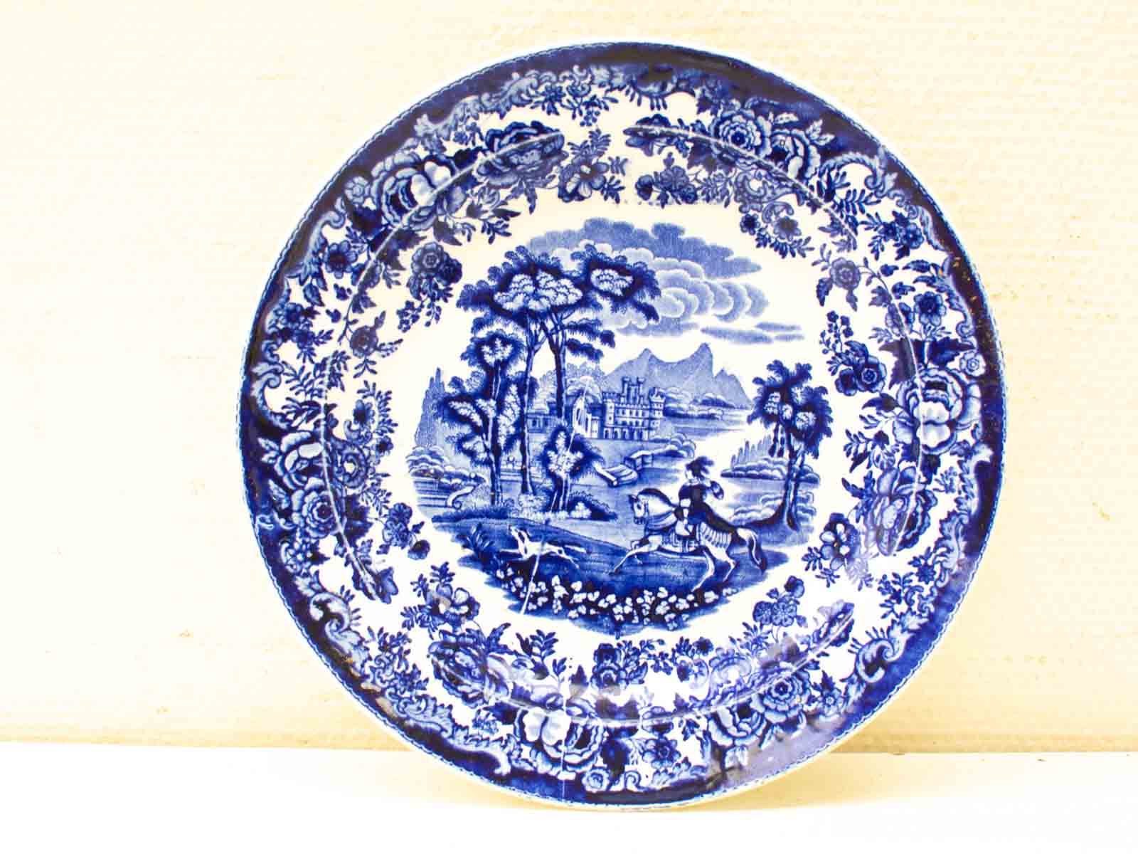 Elegant blue and white decorative plate showcasing a scenic landscape with horseback rider and floral border.