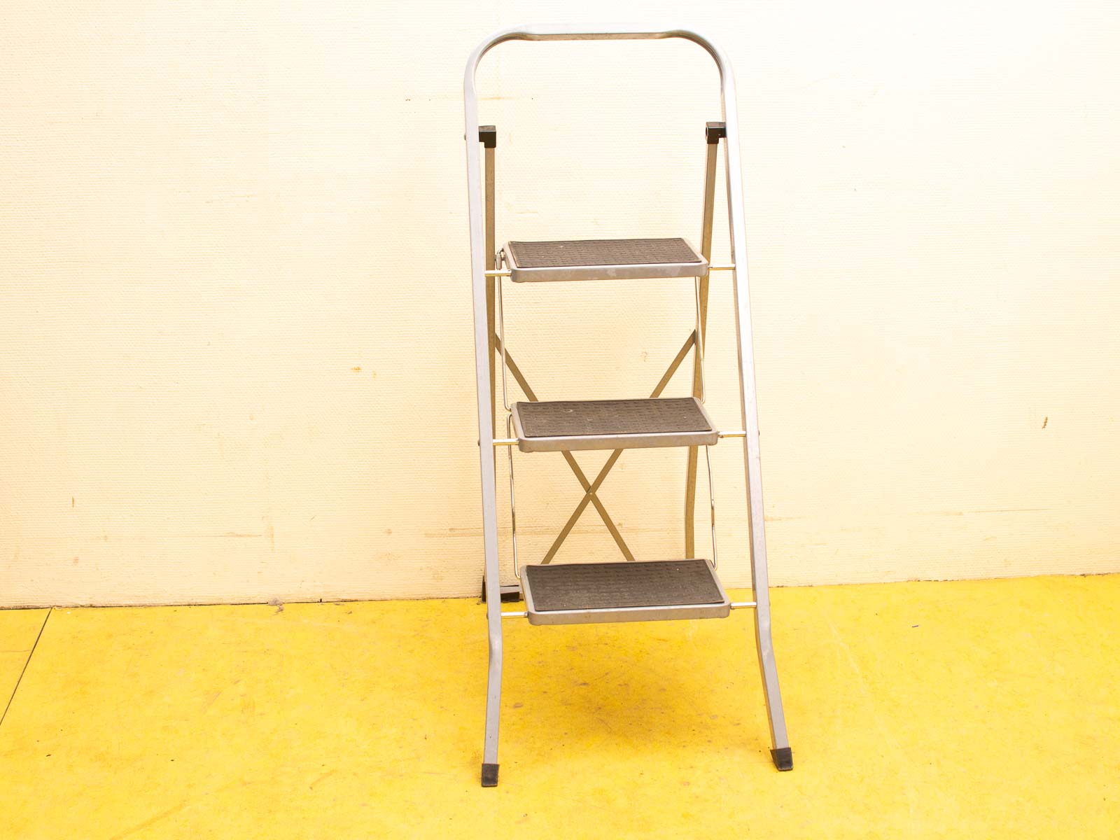 Stylish three-step ladder on bright yellow floor, ideal for home improvement tasks.