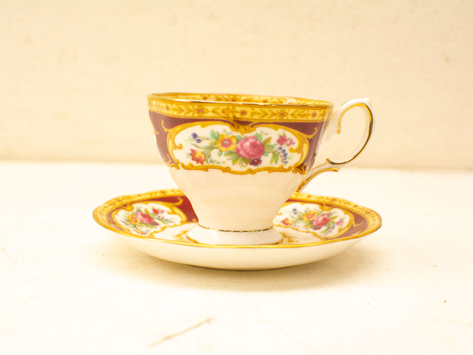 Elegant maroon tea cup and saucer with floral designs and gold accents, perfect for collectors.