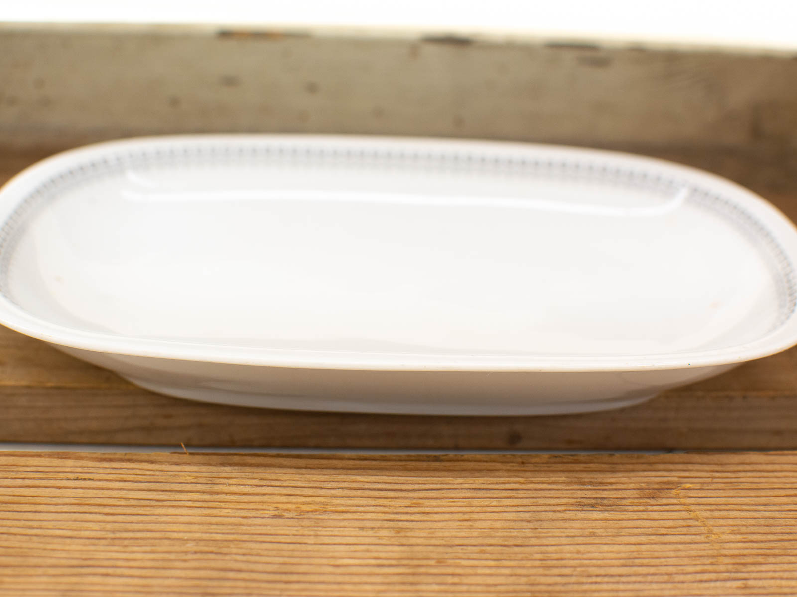 Elegant white porcelain serving dish with decorative rim on rustic wooden surface. Perfect for dining.