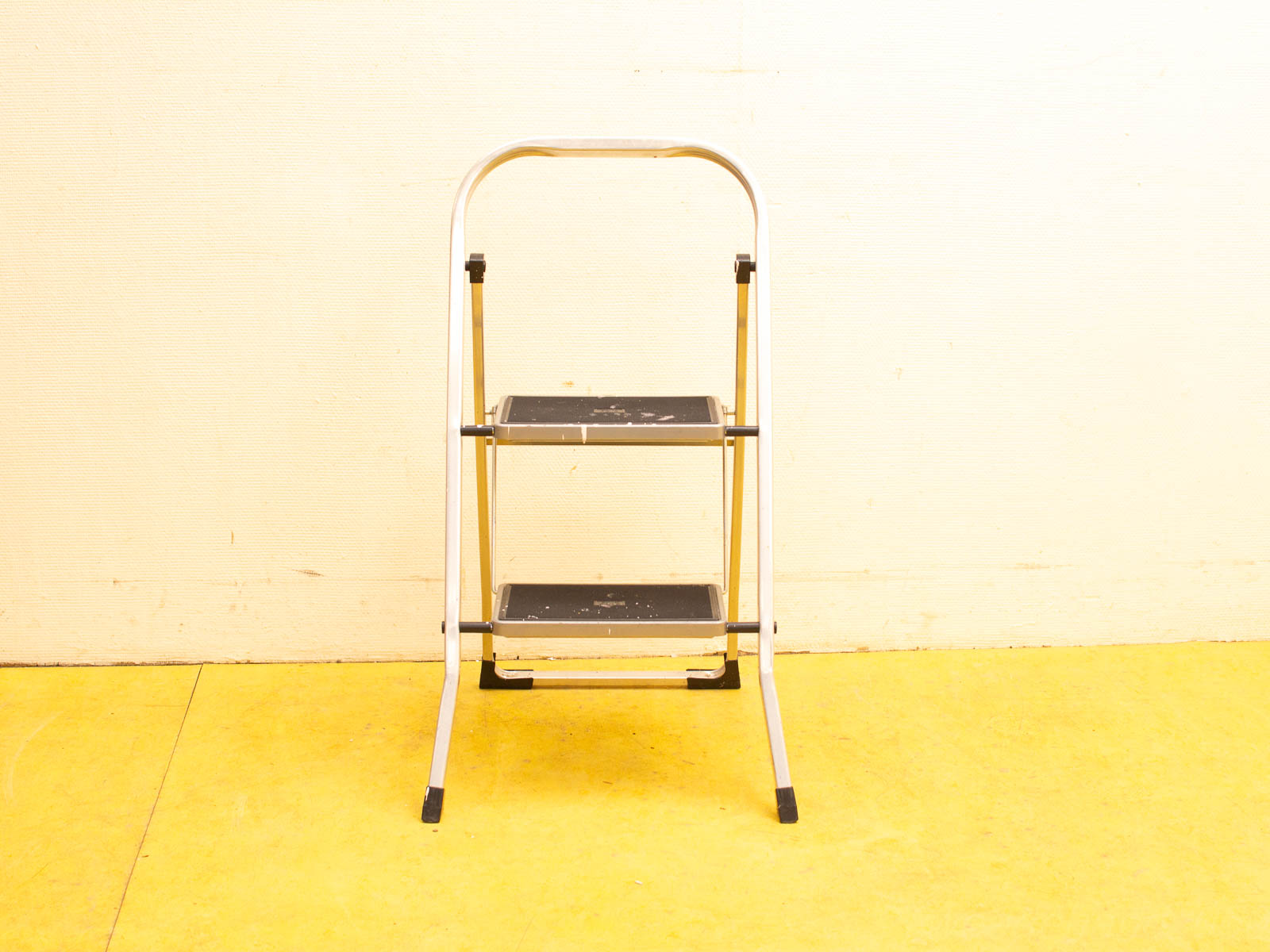 Sleek aluminum step ladder against a textured yellow wall, perfect for everyday tasks.