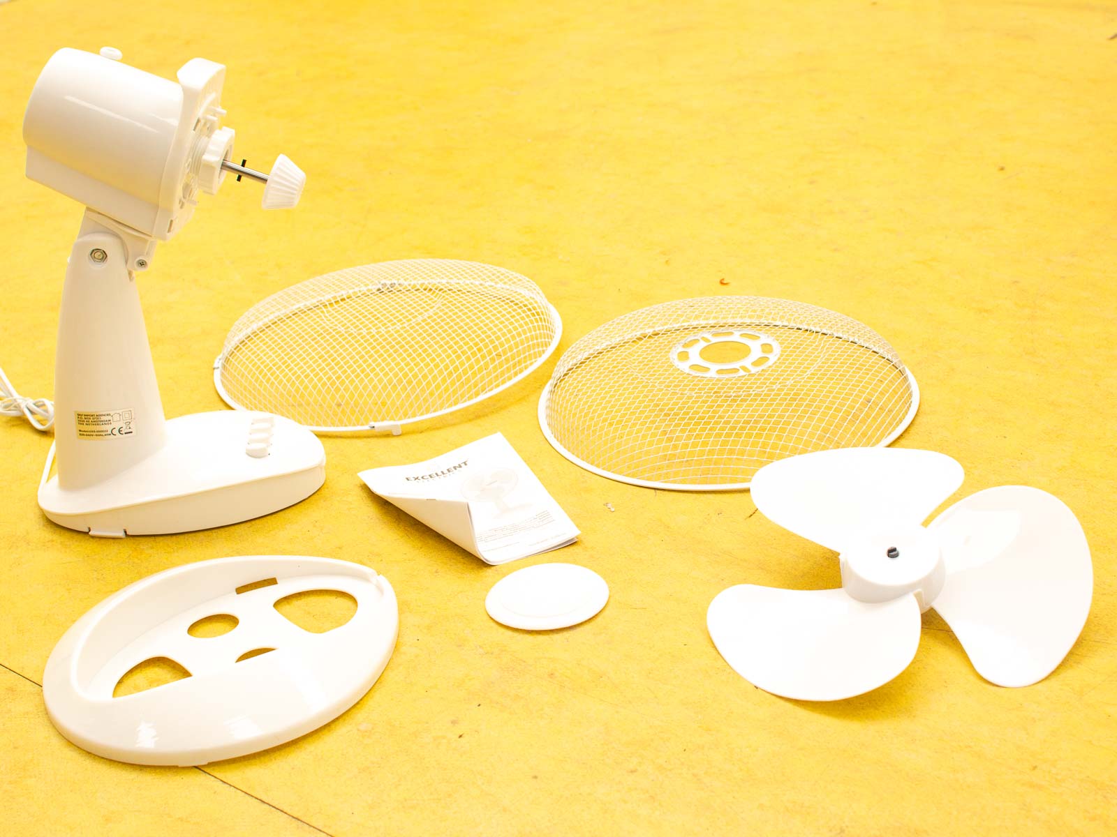 Disassembled table fan parts on a bright yellow background, showcasing modern design and assembly ease.