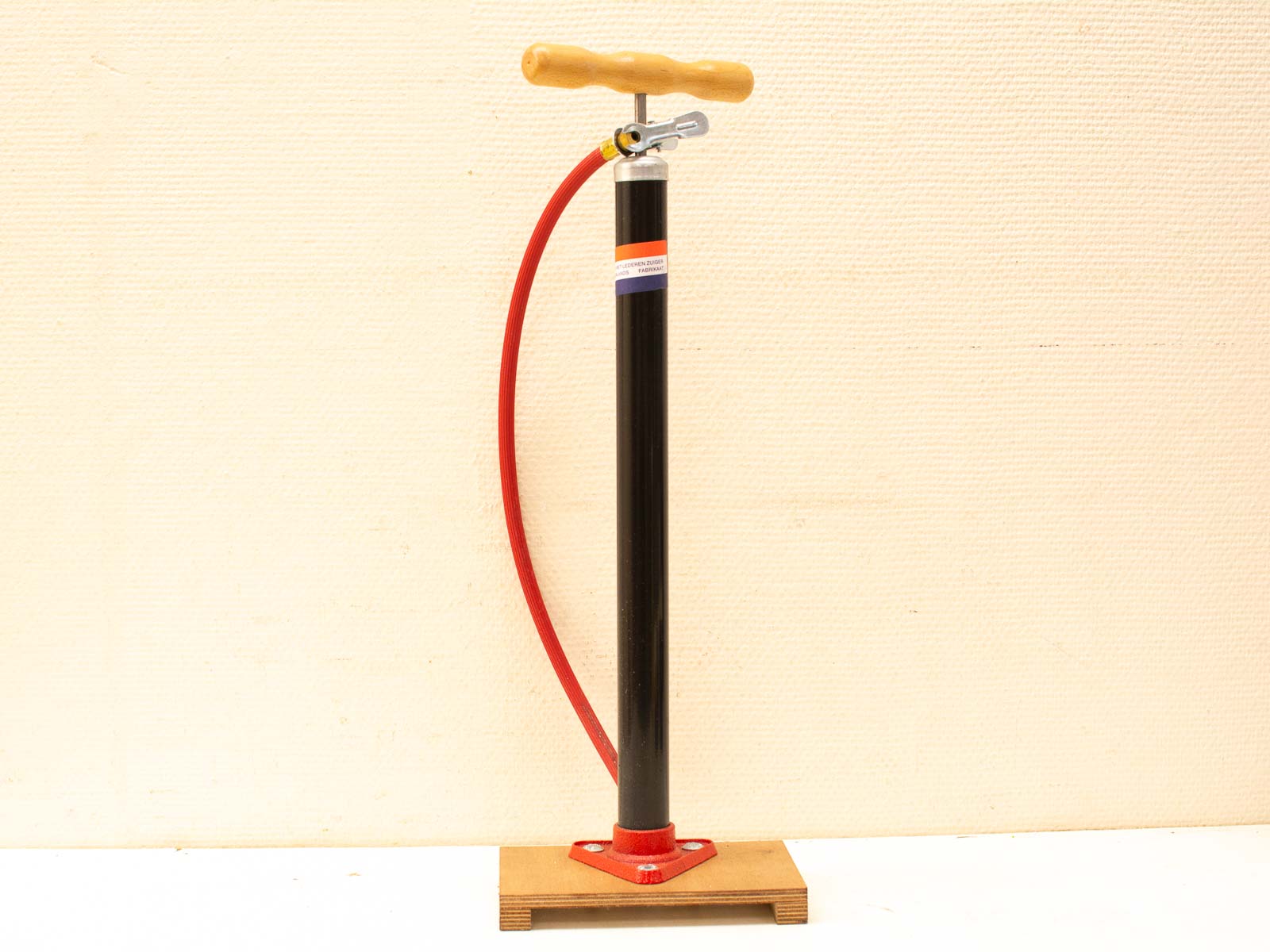 Vintage bicycle pump with a wooden handle, red hose, and sturdy black barrel for tire inflation.