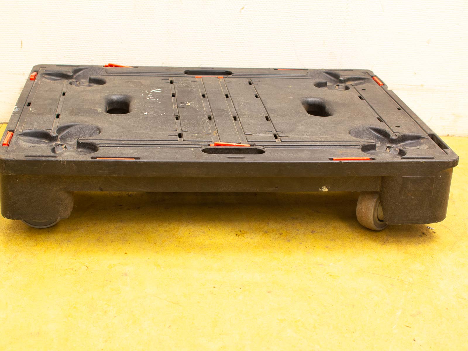 Used black plastic pallet with wheels, ideal for transport, showcasing stability and durability.