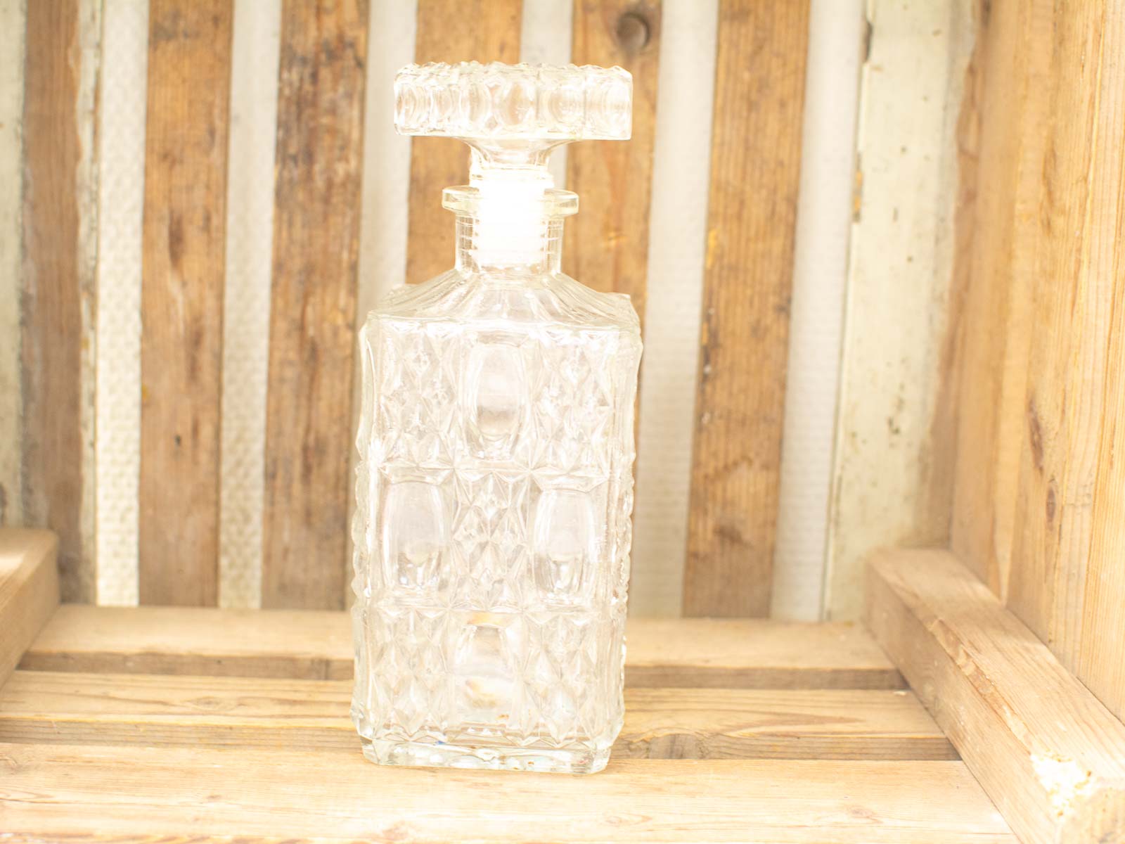 Elegant glass decanter with ornate stopper on rustic wood, perfect for home decor.