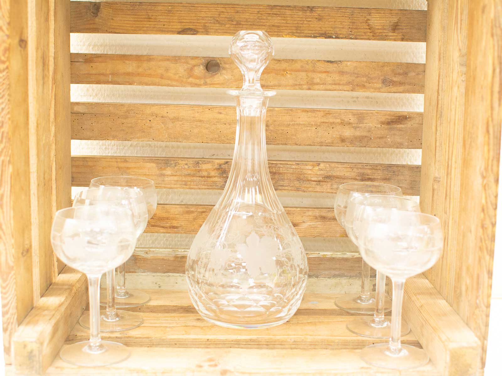 Elegant glass decanter and coupe glasses in rustic wooden crate for stylish home decor.