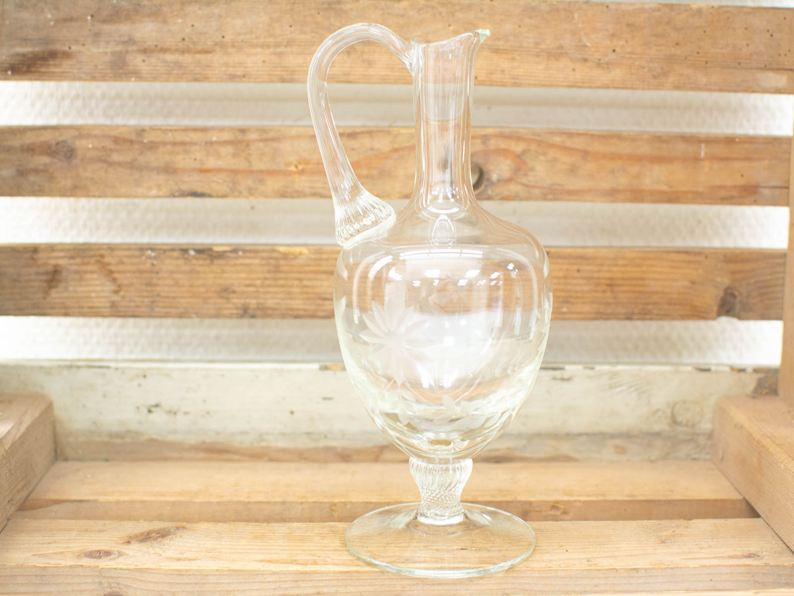 Elegant glass pitcher on rustic wood, perfect for serving or as a decorative centerpiece.