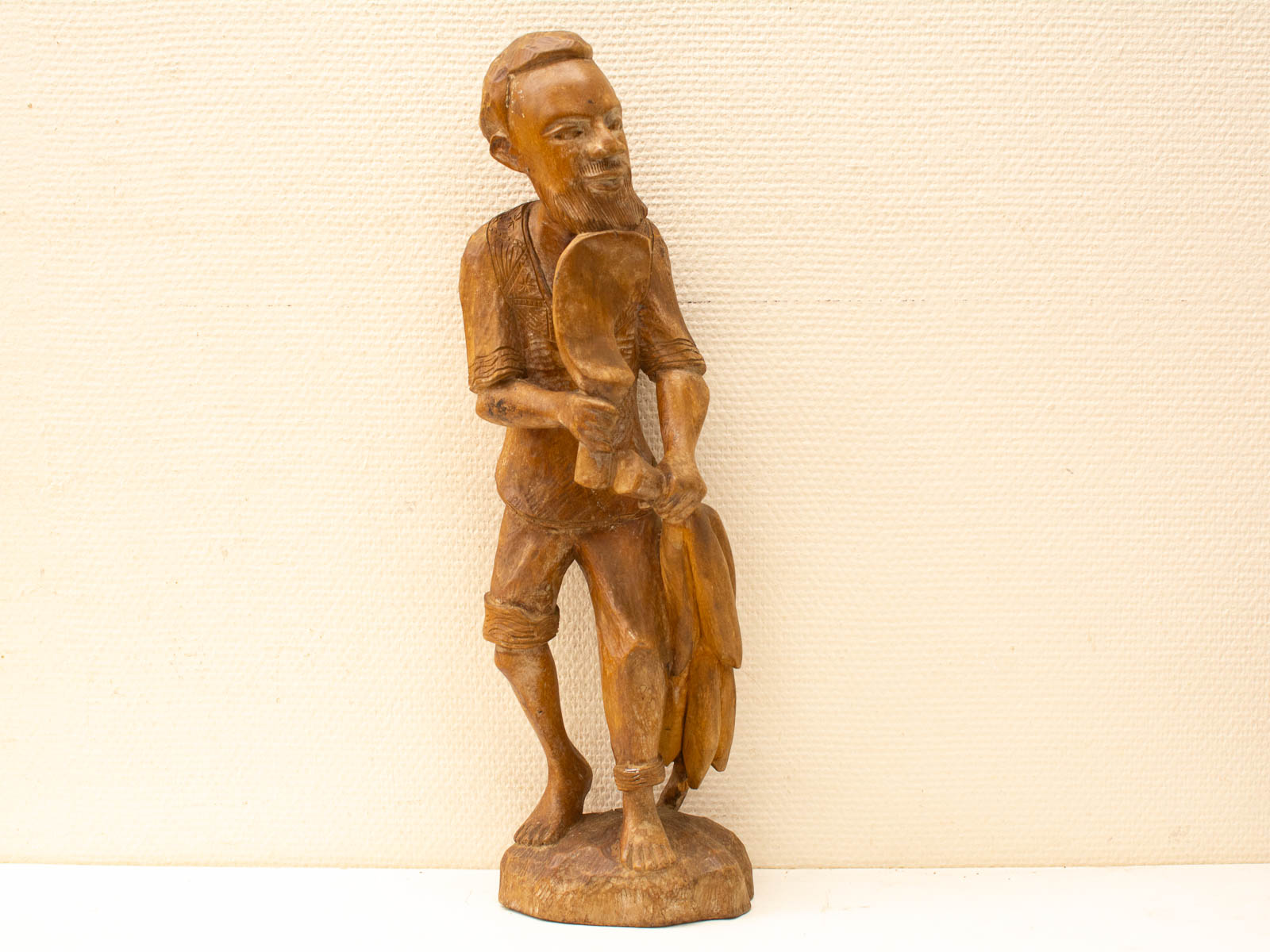 Intricately carved wooden statue of a harvester with bananas and a spoon, showcasing cultural heritage.