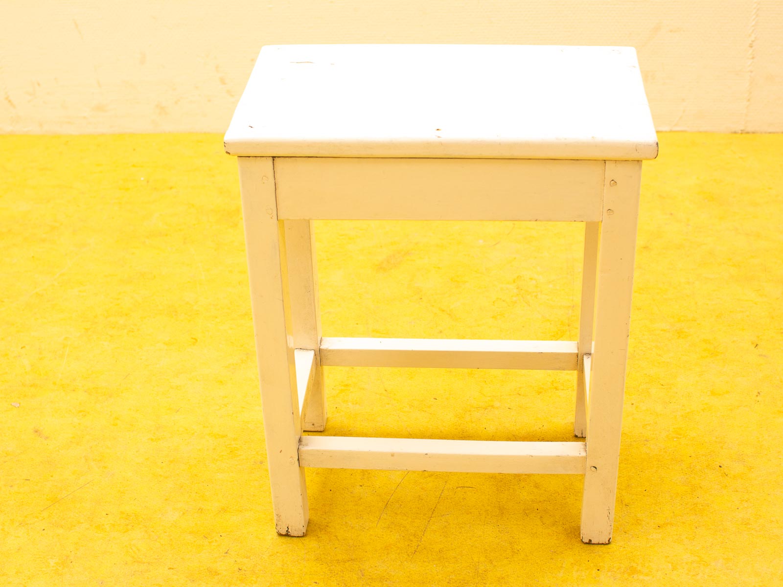 Charming white wooden stool on a bright yellow floor, perfect for any decor style.