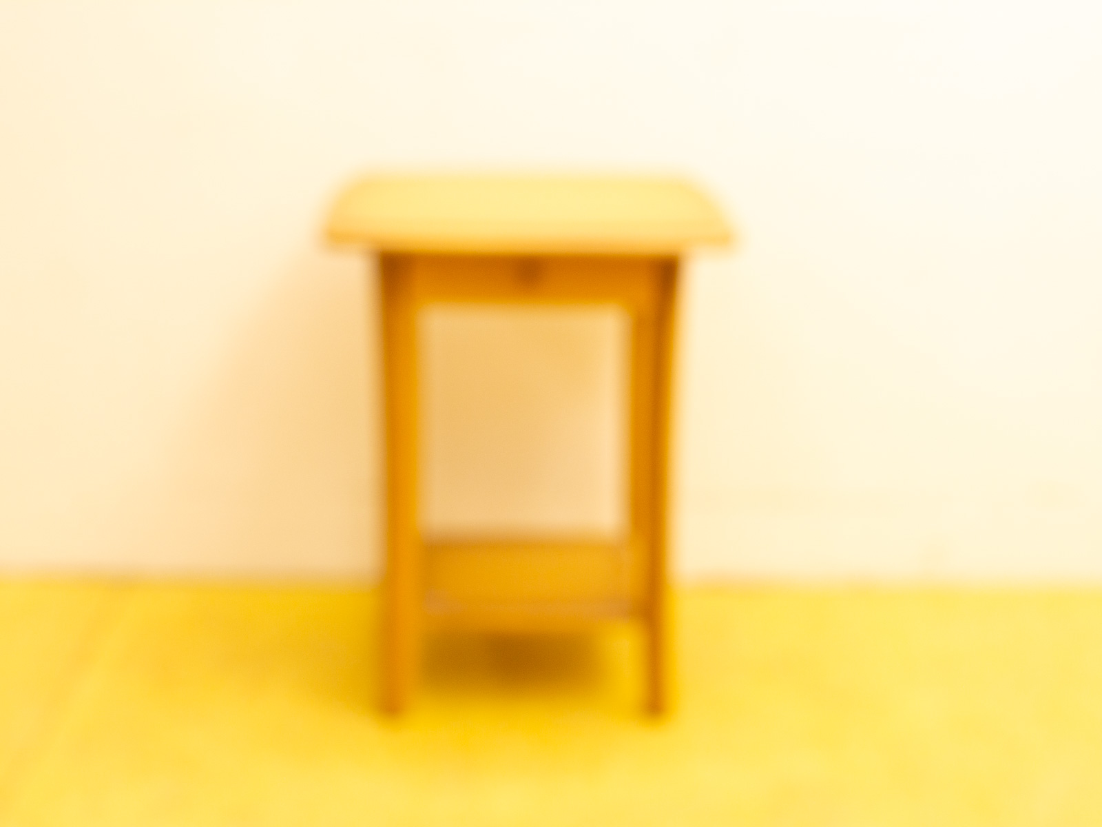 Charming wooden table with drawer on bright yellow floor, adding warmth and style to any space.