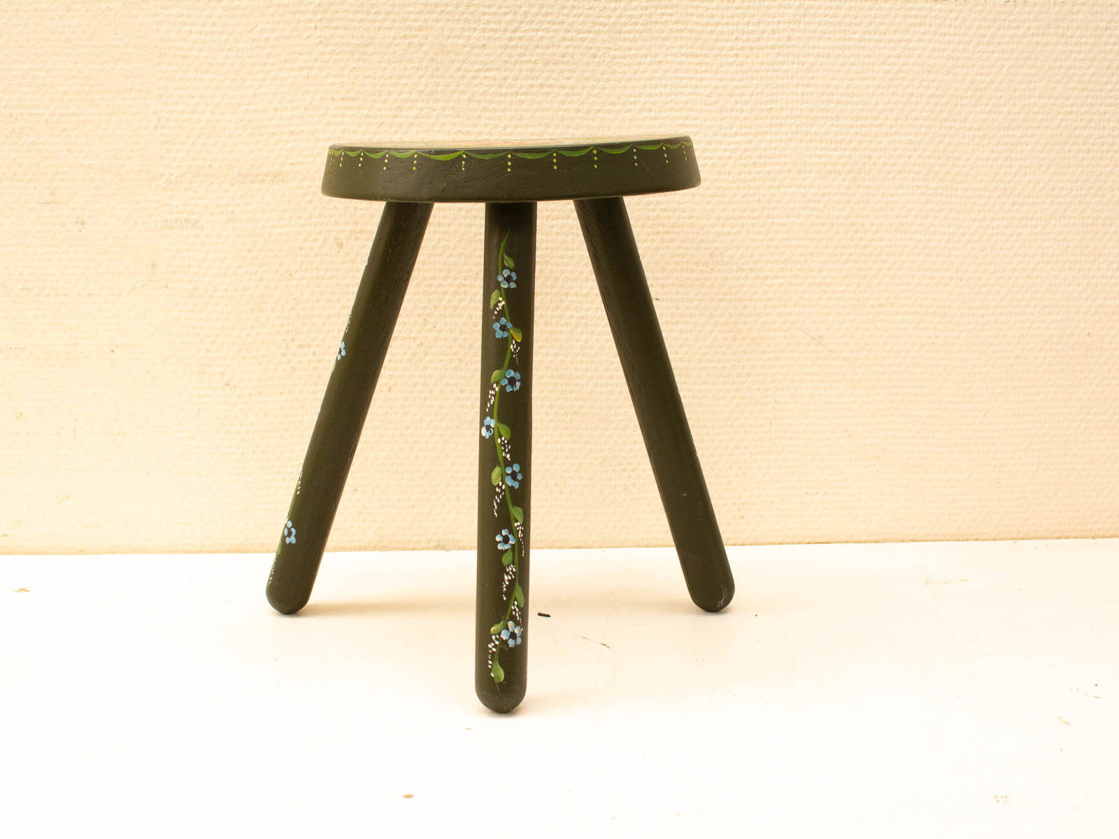 Charming green three-legged stool with floral accents, perfect for rustic decor.