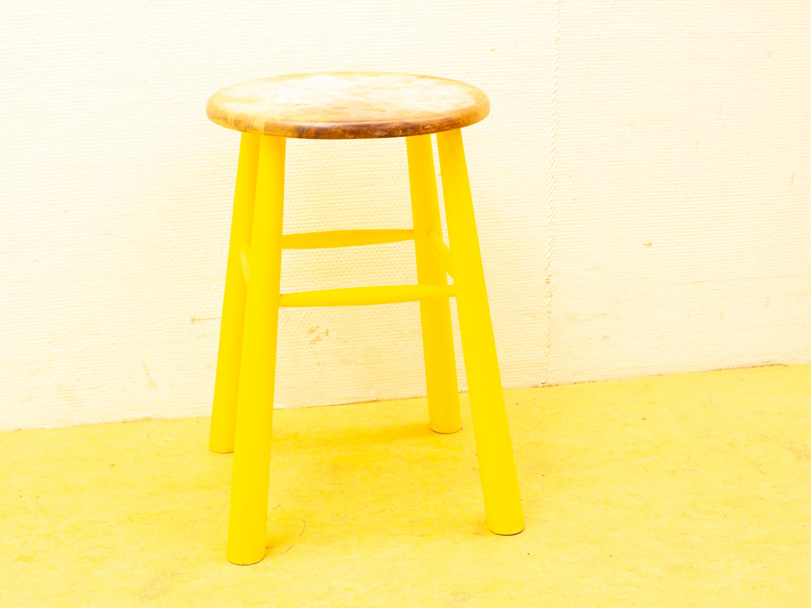 Vibrant vintage stool with yellow legs and natural wood seat, perfect for adding color.