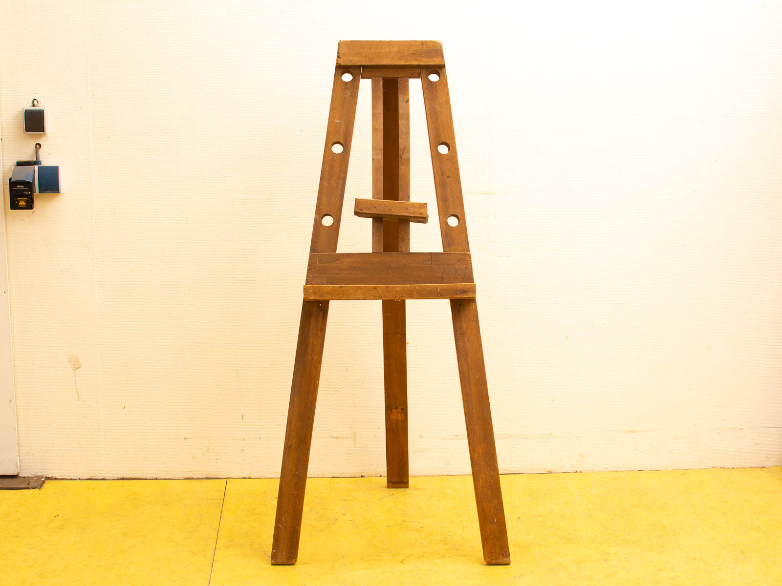 Rustic wooden easel in bright studio with yellow floor, perfect for creative inspiration.