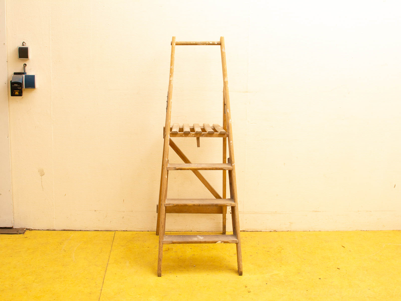 Wooden step ladder against a cream wall and bright yellow floor, ideal for practical tasks.