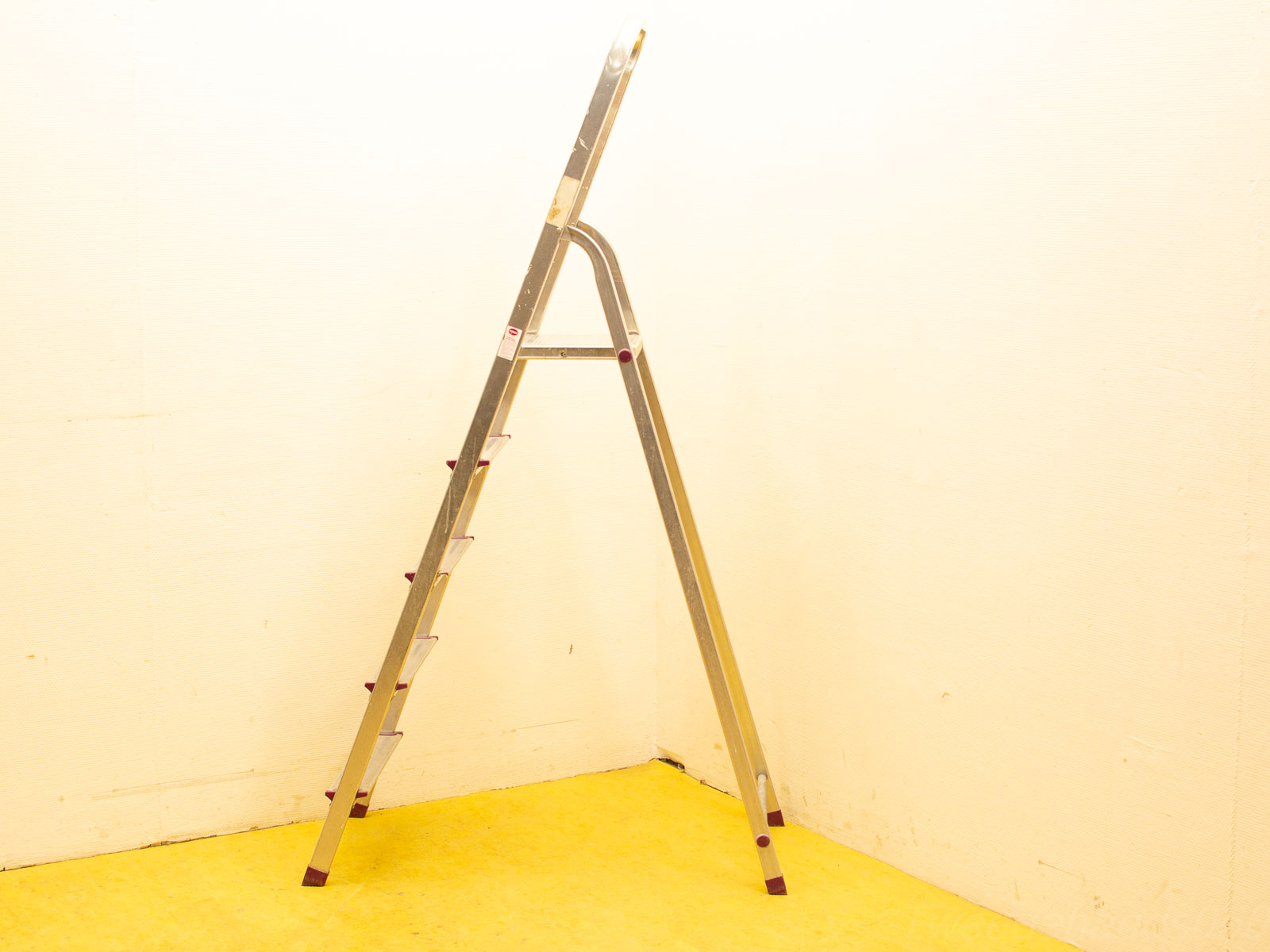 Stylish aluminum ladder against a white wall, featuring six sturdy steps on a yellow floor.