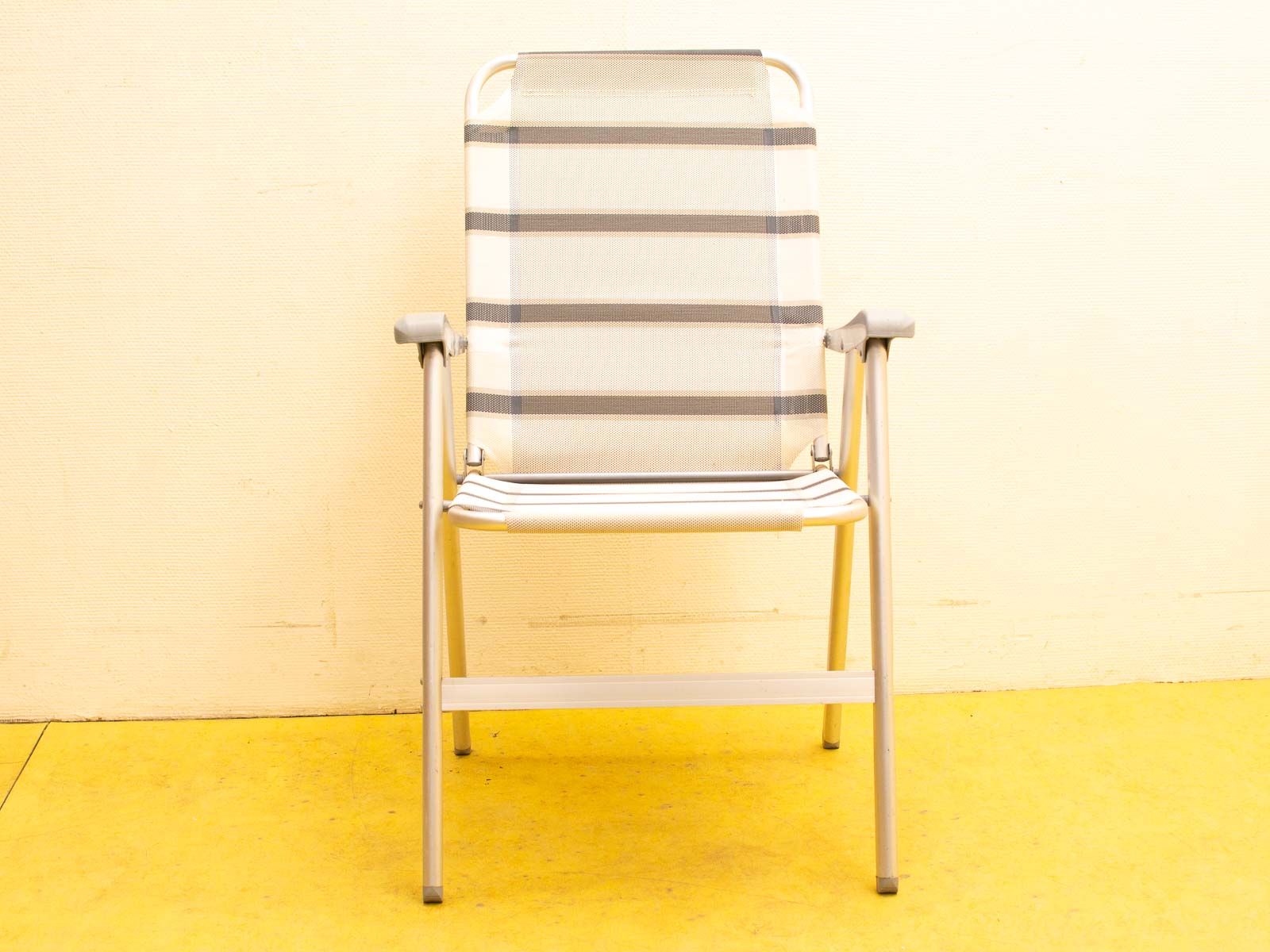 Modern folding chair with striped fabric on vibrant yellow floor, perfect for any setting.