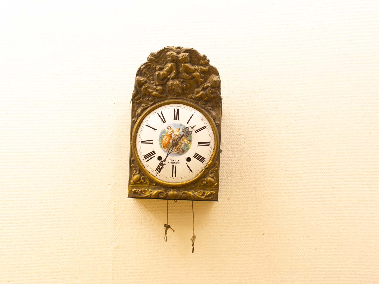 Elegant antique clock with floral carvings, Roman numerals, and a charming painted scene.