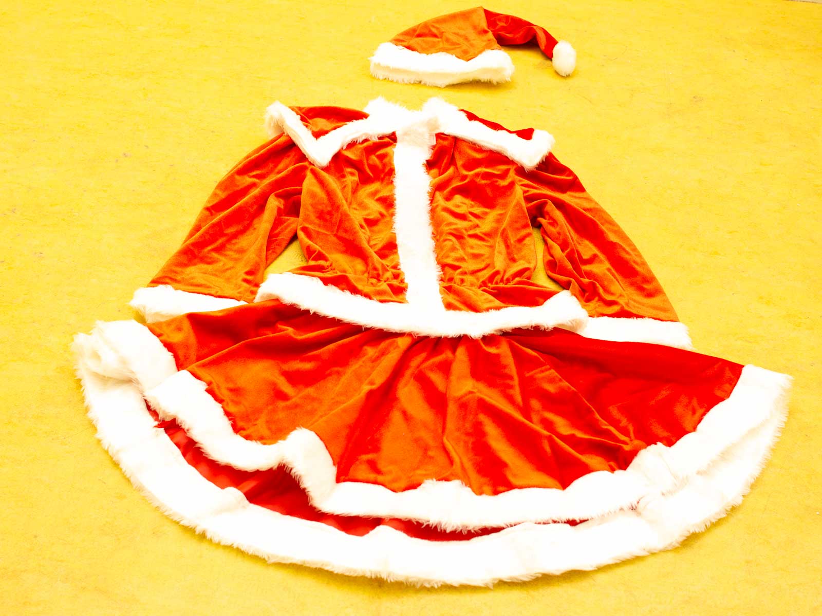 Vibrant red Christmas dress and Santa hat on a cheerful yellow background.