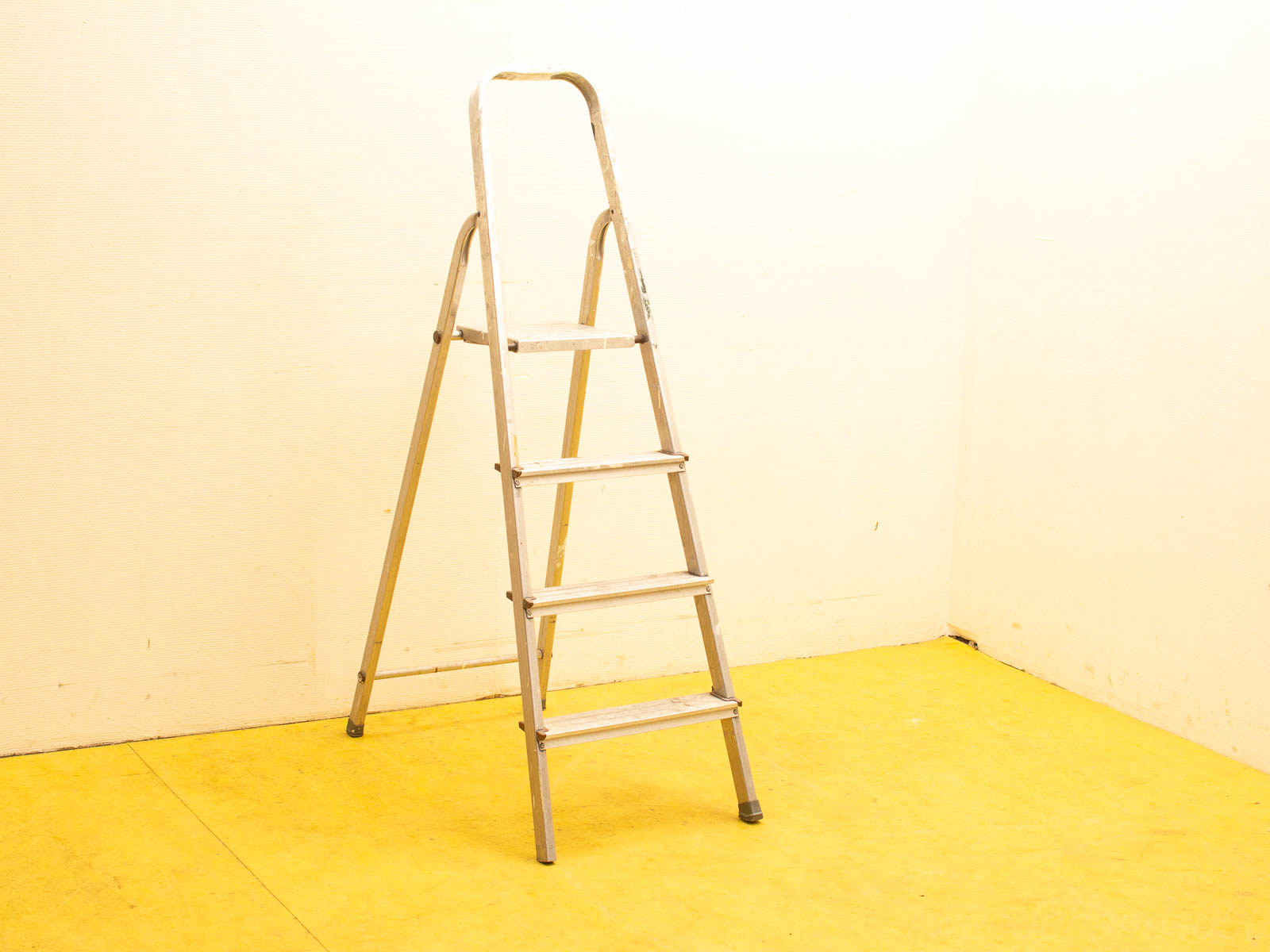 Sleek aluminum step ladder on bright yellow floor against a soft, neutral background.