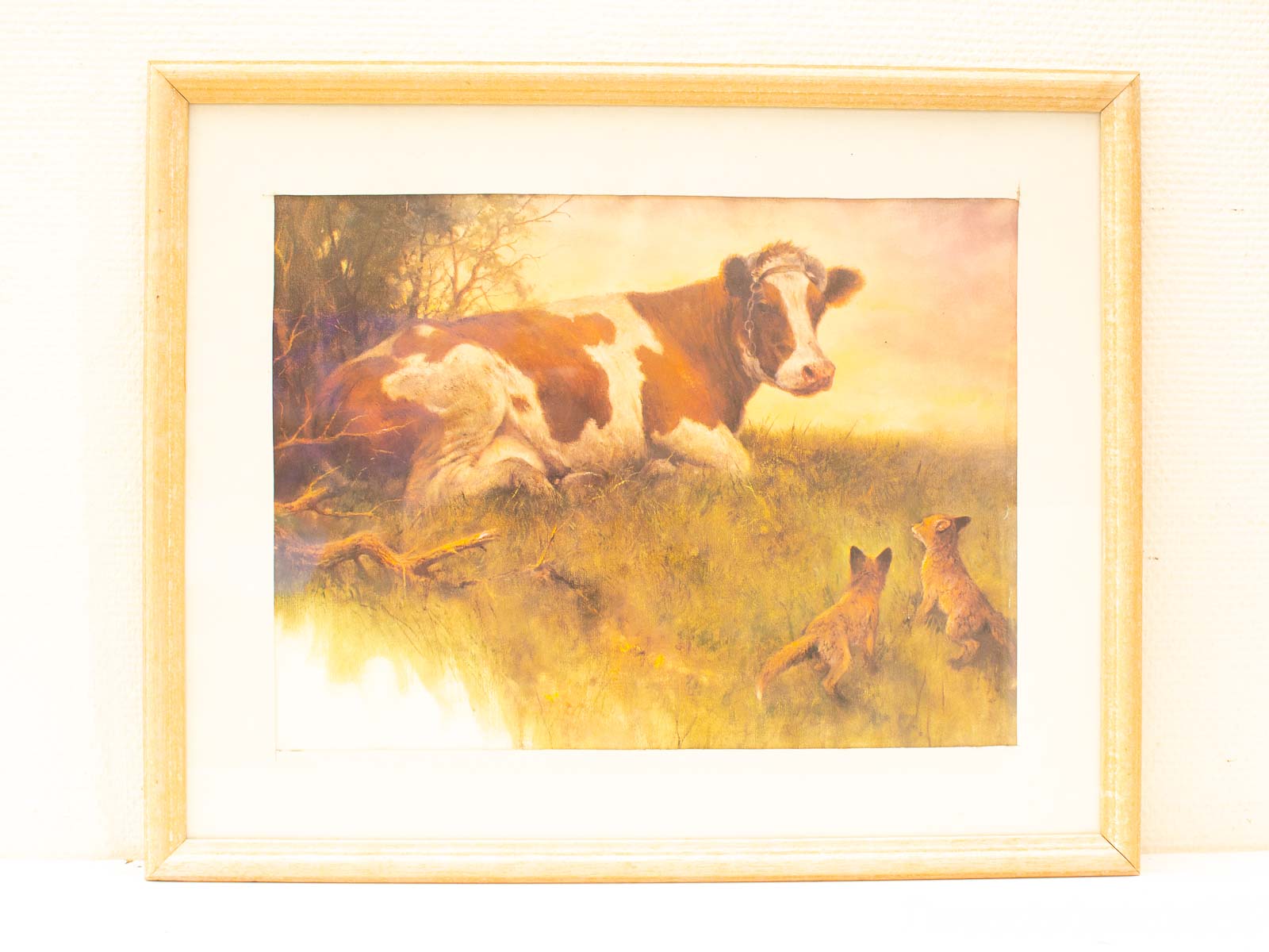 Serene scene of a resting cow with playful foxes in a peaceful green field.