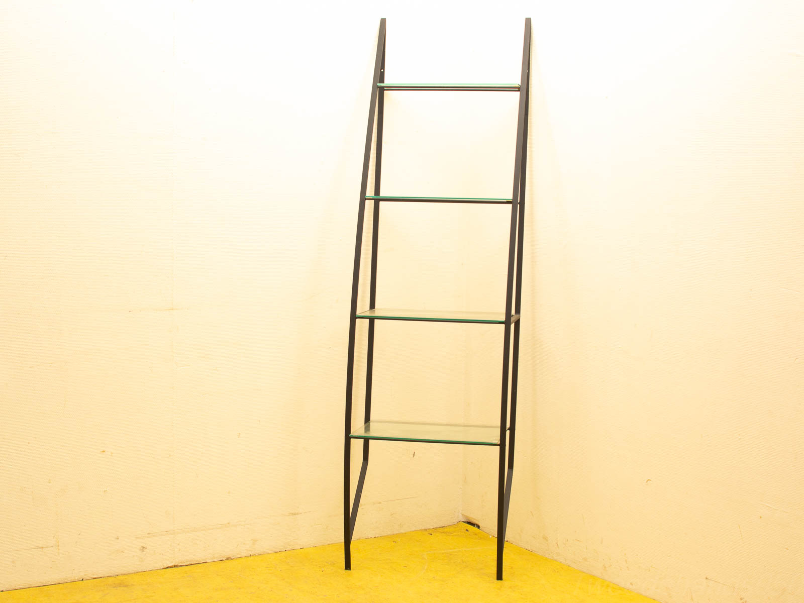 Stylish ladder shelving unit with glass shelves against a textured wall and vibrant yellow floor.