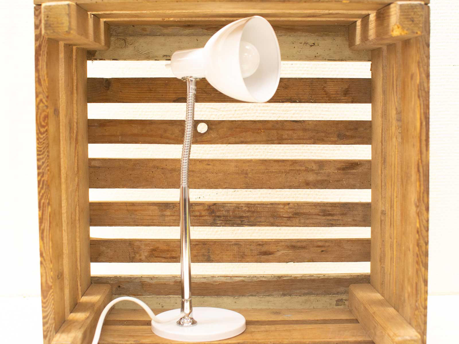 Modern desk lamp in rustic wooden crate, blending sleek design with cozy charm.