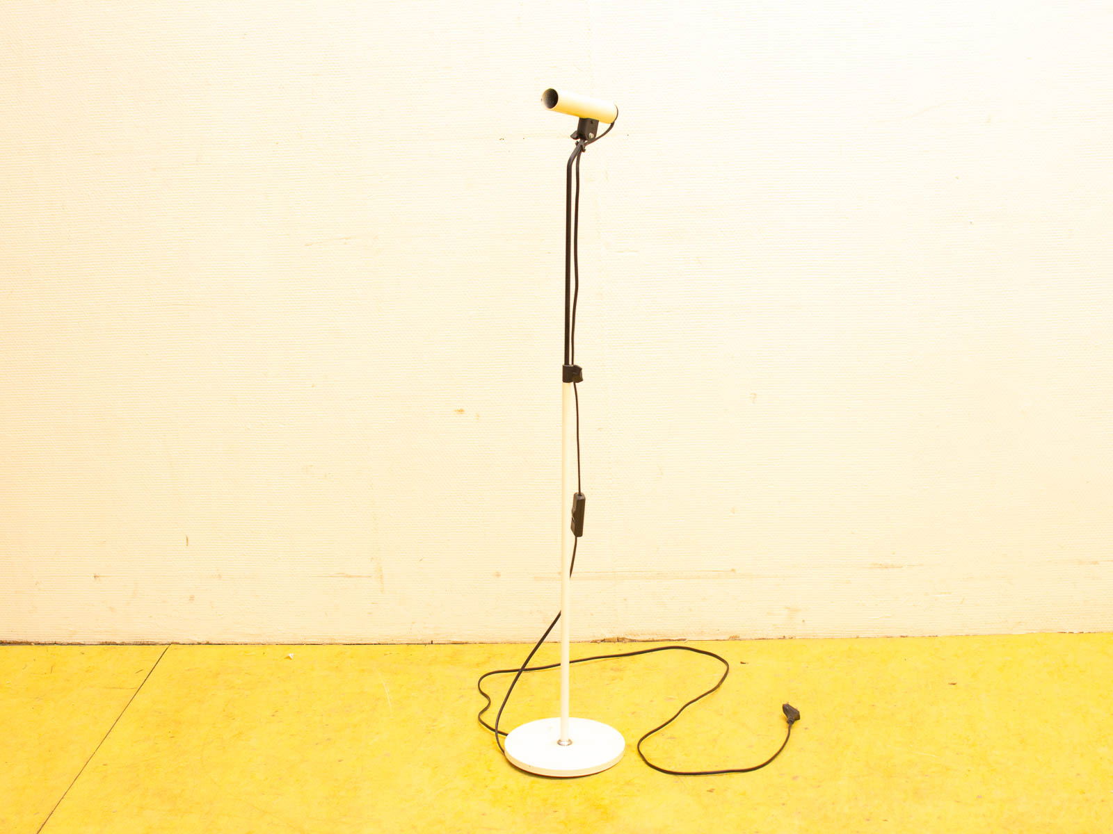 Sleek microphone on white stand against light wall and vibrant yellow floor. Ideal for audio use.