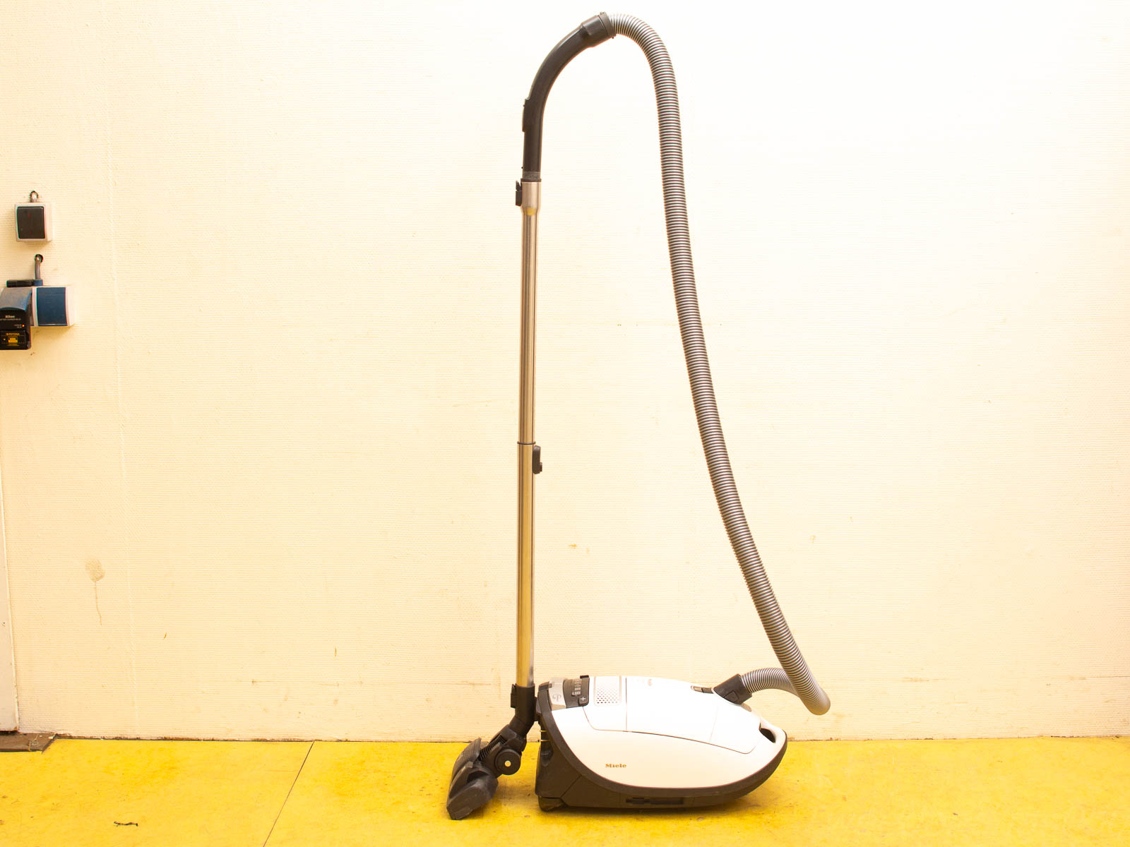 Sleek white Miele canister vacuum cleaner on a vibrant yellow floor, combining style and functionality.