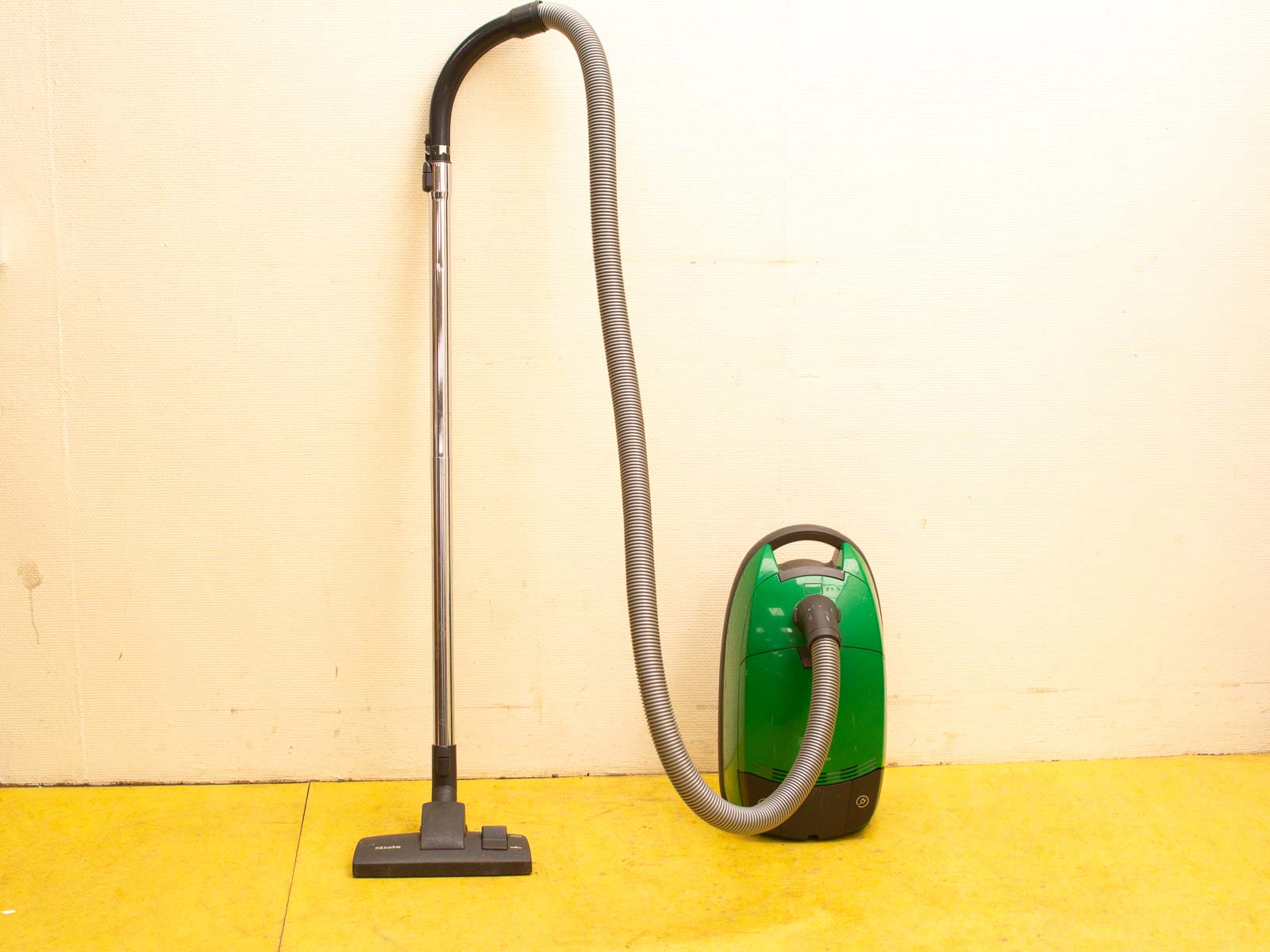 Vibrant green vacuum cleaner with flexible hose on cheerful yellow floor, ideal for efficient cleaning.