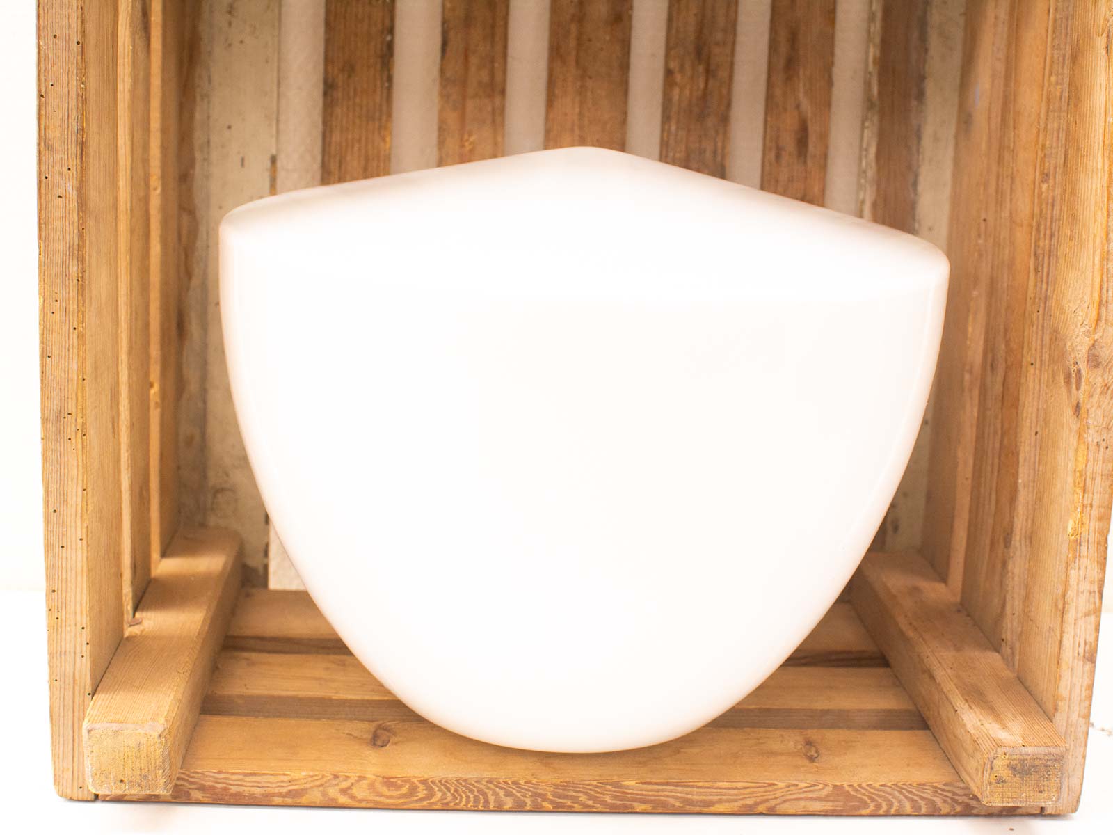 Sleek white sculpture in rustic wooden crate, blending modern design with natural warmth.