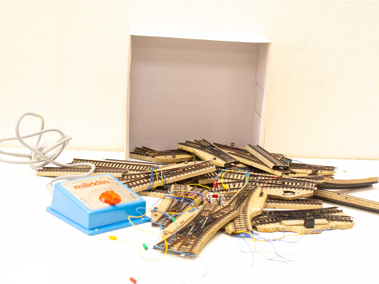 Model train tracks and Märklin control unit arranged creatively around a storage box.