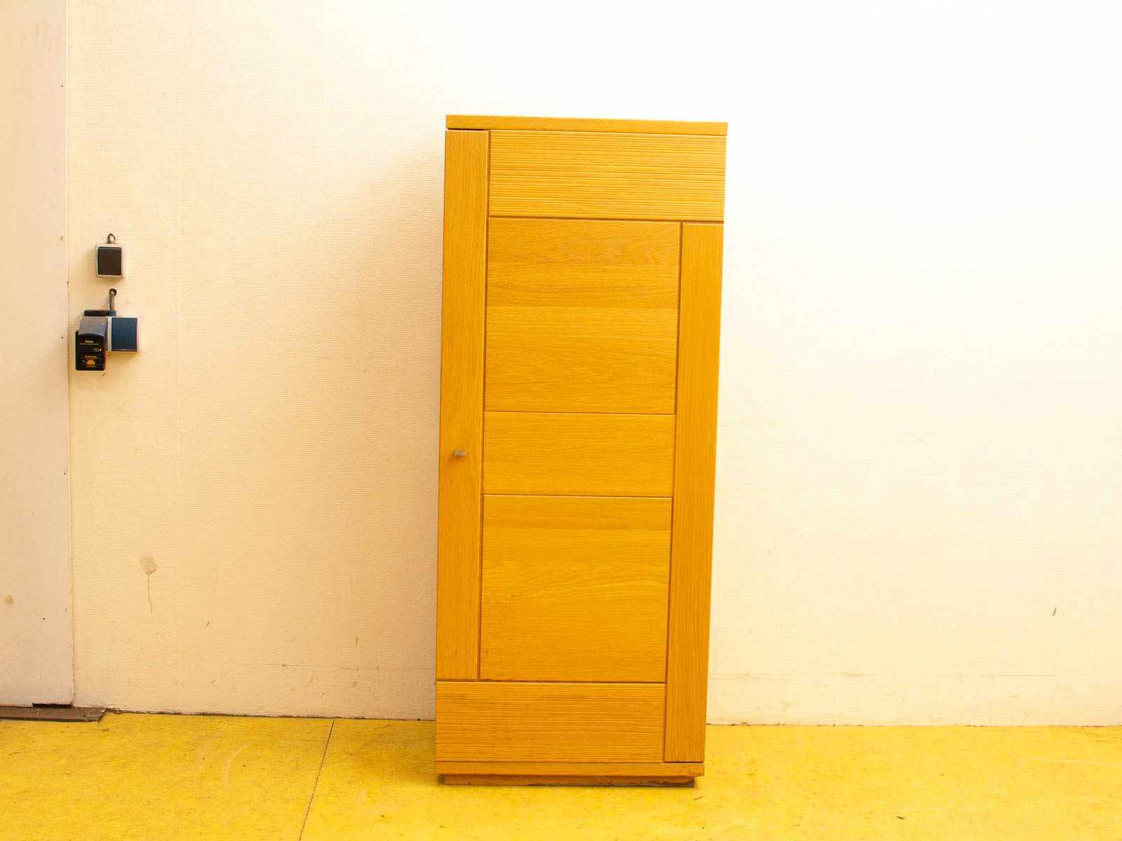 Modern wooden cabinet with drawers on a vibrant yellow floor in a minimalist setting.