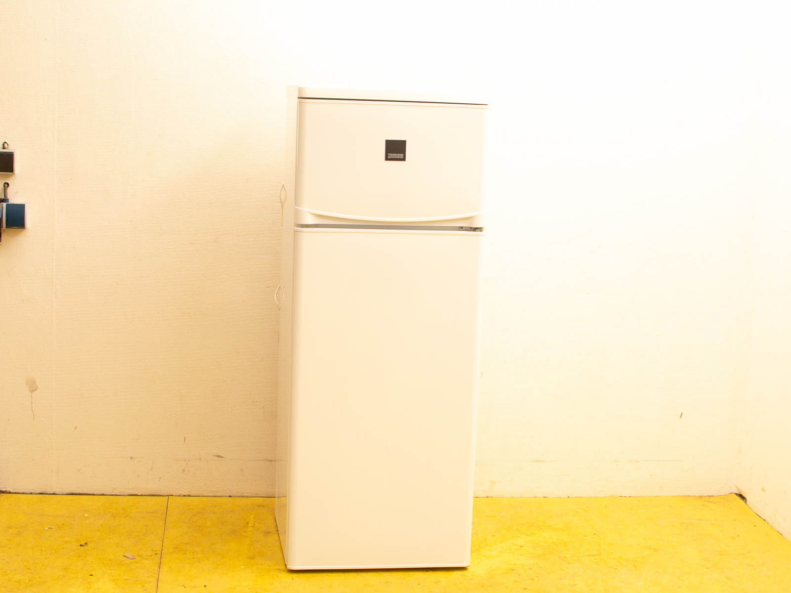 Modern white refrigerator with top freezer, set in a bright, minimalist kitchen space.