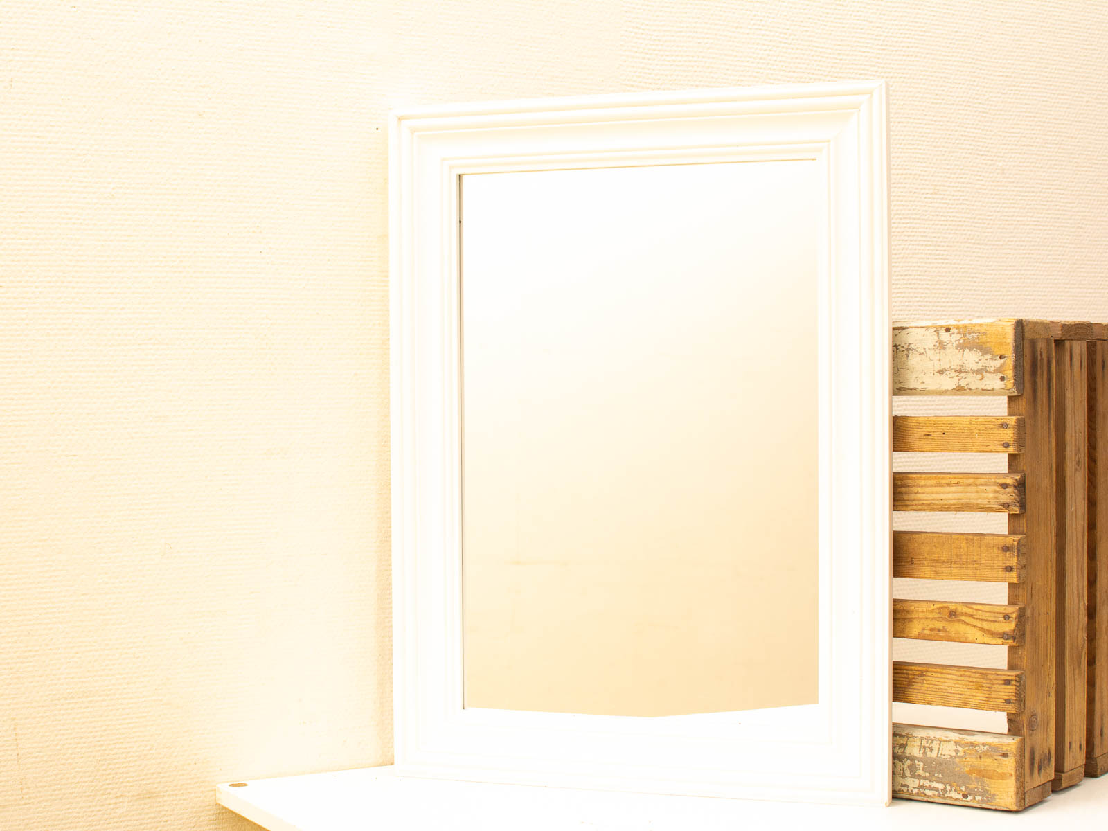 Elegant mirror with ornate frame beside rustic wooden crate in serene, minimalistic setting.