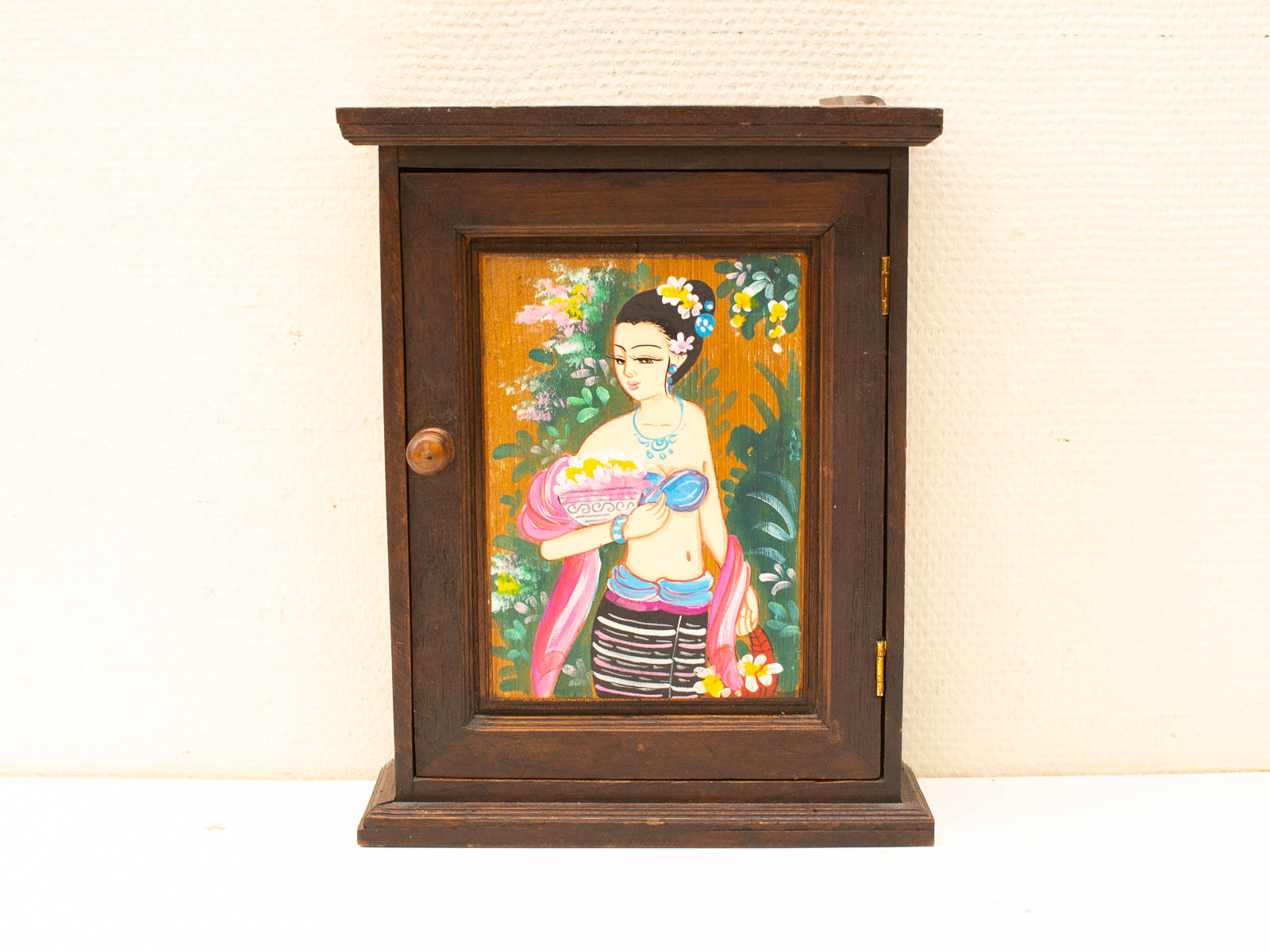 Vintage wooden cabinet with colorful painted panel of a woman among flowers and foliage.