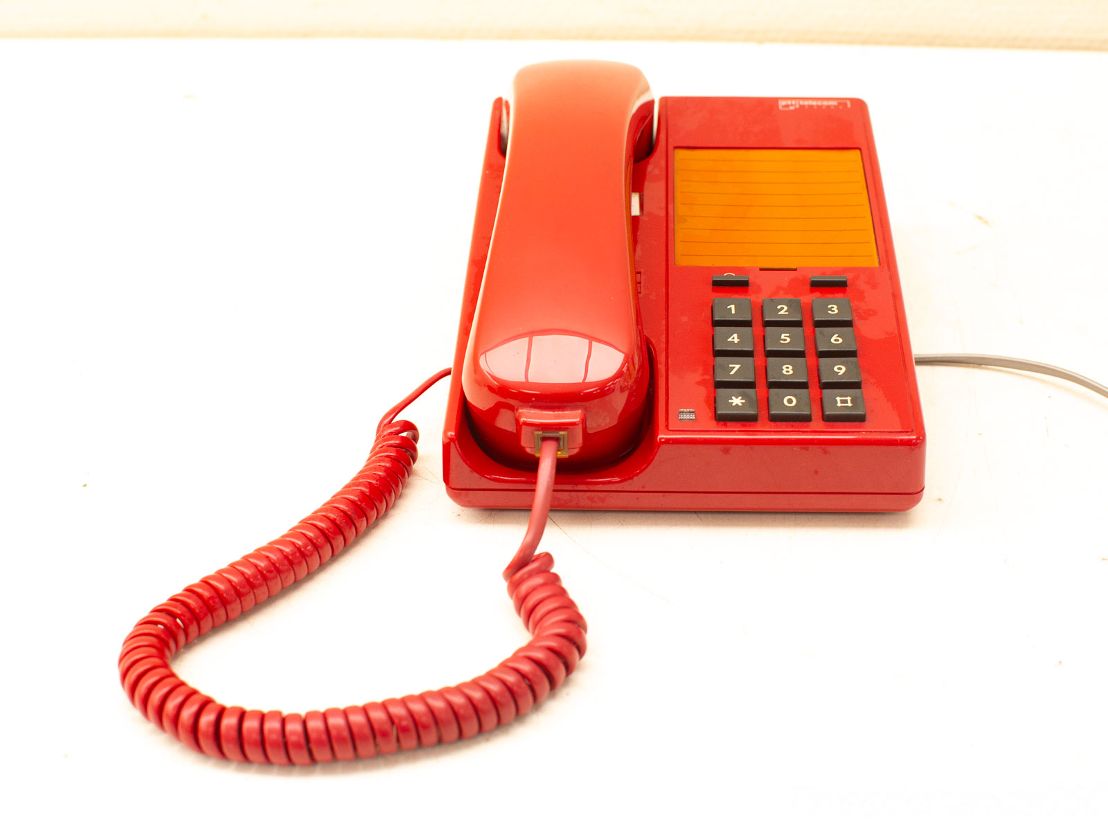 Vibrant red rotary telephone with notepad, coiled cord, and classic vintage appeal.