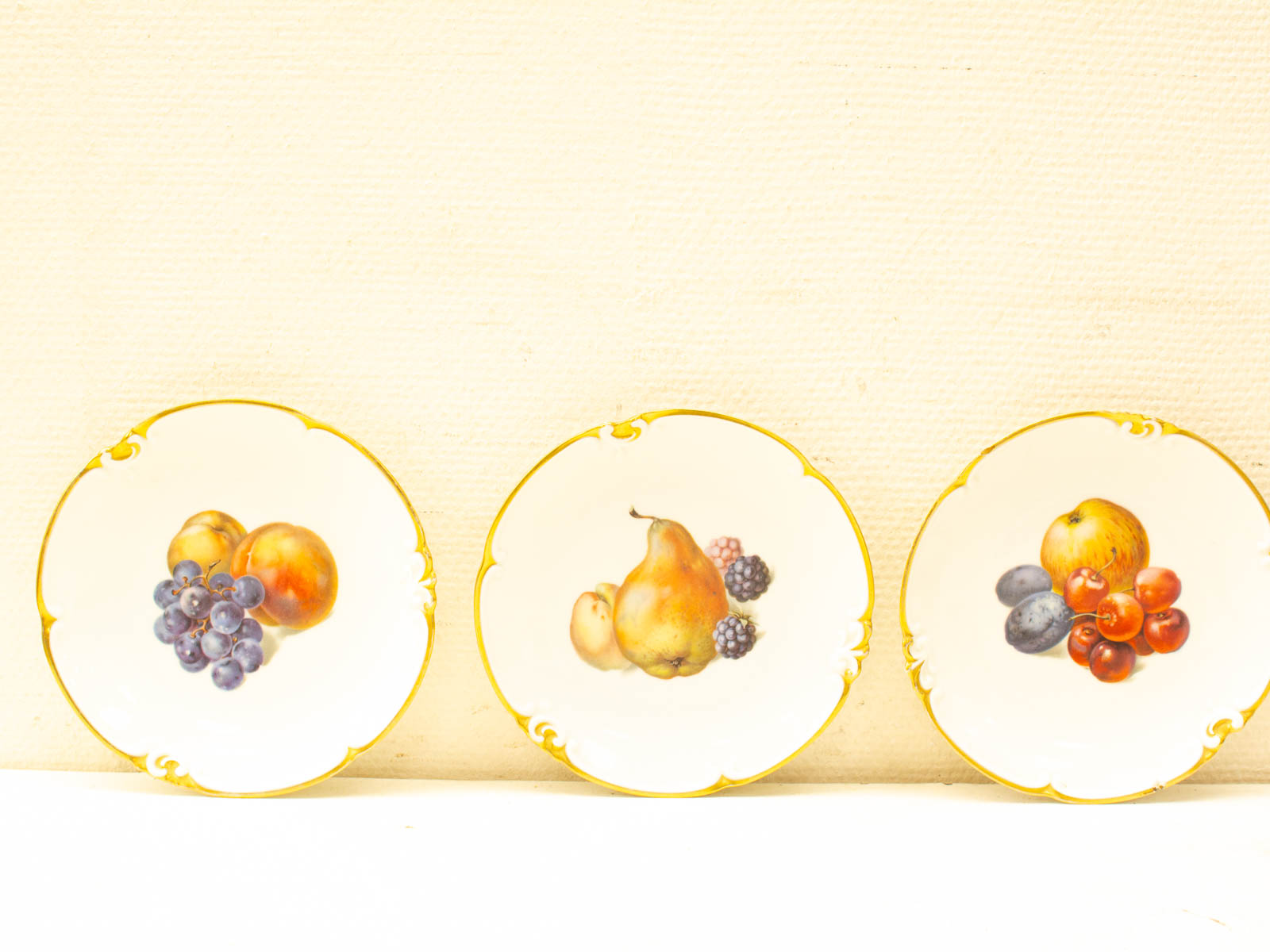 Elegant vintage porcelain plates with vibrant fruit paintings and golden rims for display or dining.