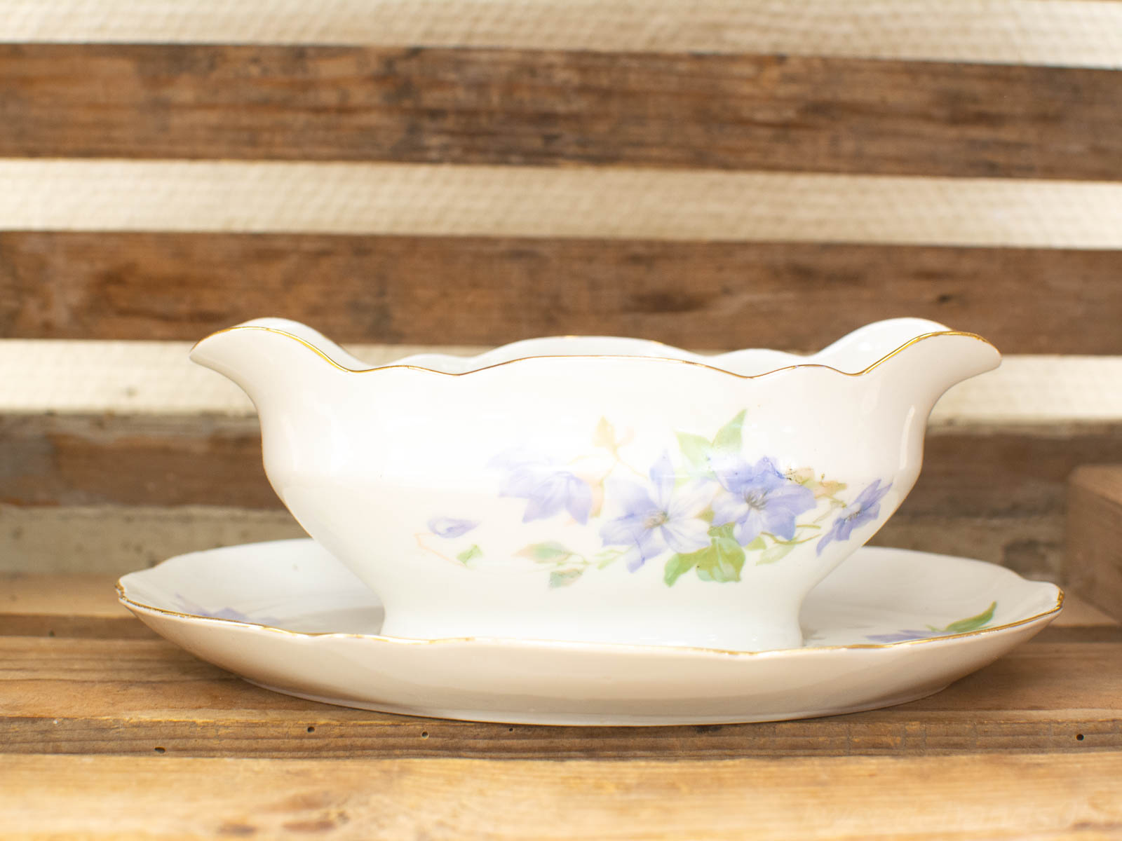 Elegant vintage porcelain gravy boat with floral design and gold accents on matching saucer.