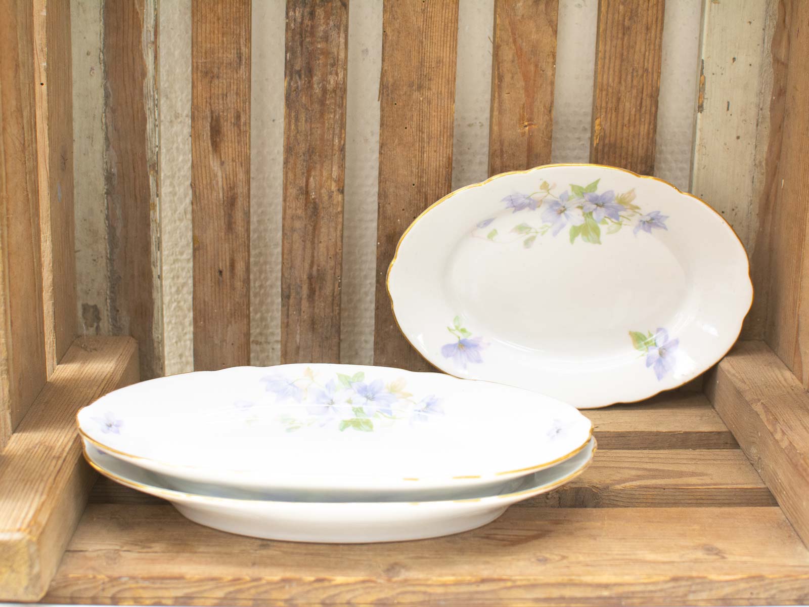 Elegant porcelain platters in rustic wooden crate with pastel floral designs for charming gatherings.