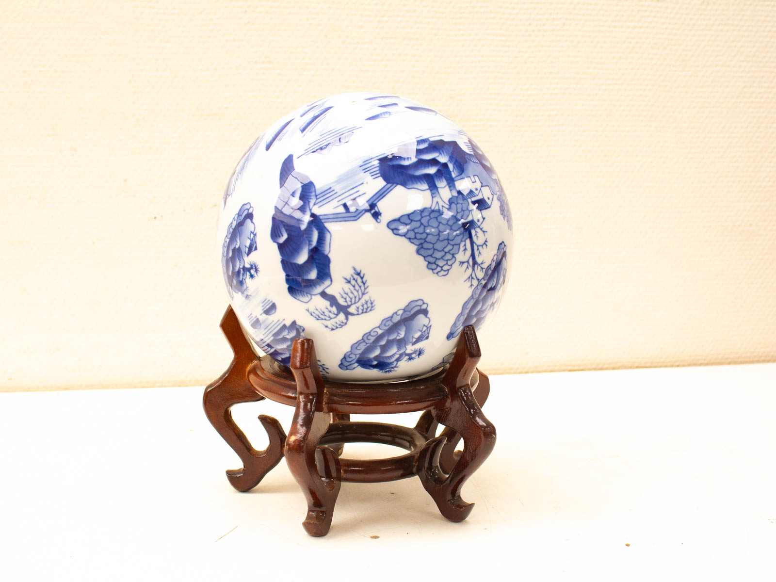 Elegant ceramic sphere with blue designs on a dark wooden stand, showcasing exquisite craftsmanship.