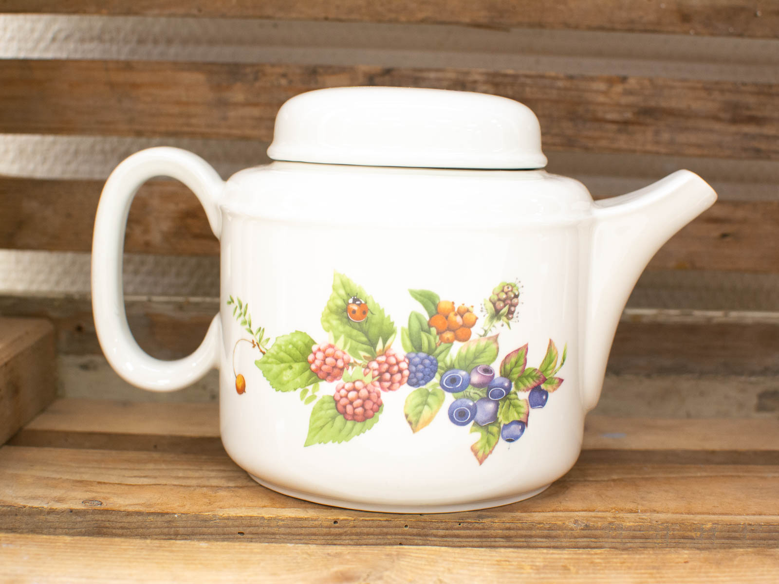 Charming ceramic teapot with berry design and ladybug, perfect for kitchen decor and gatherings.