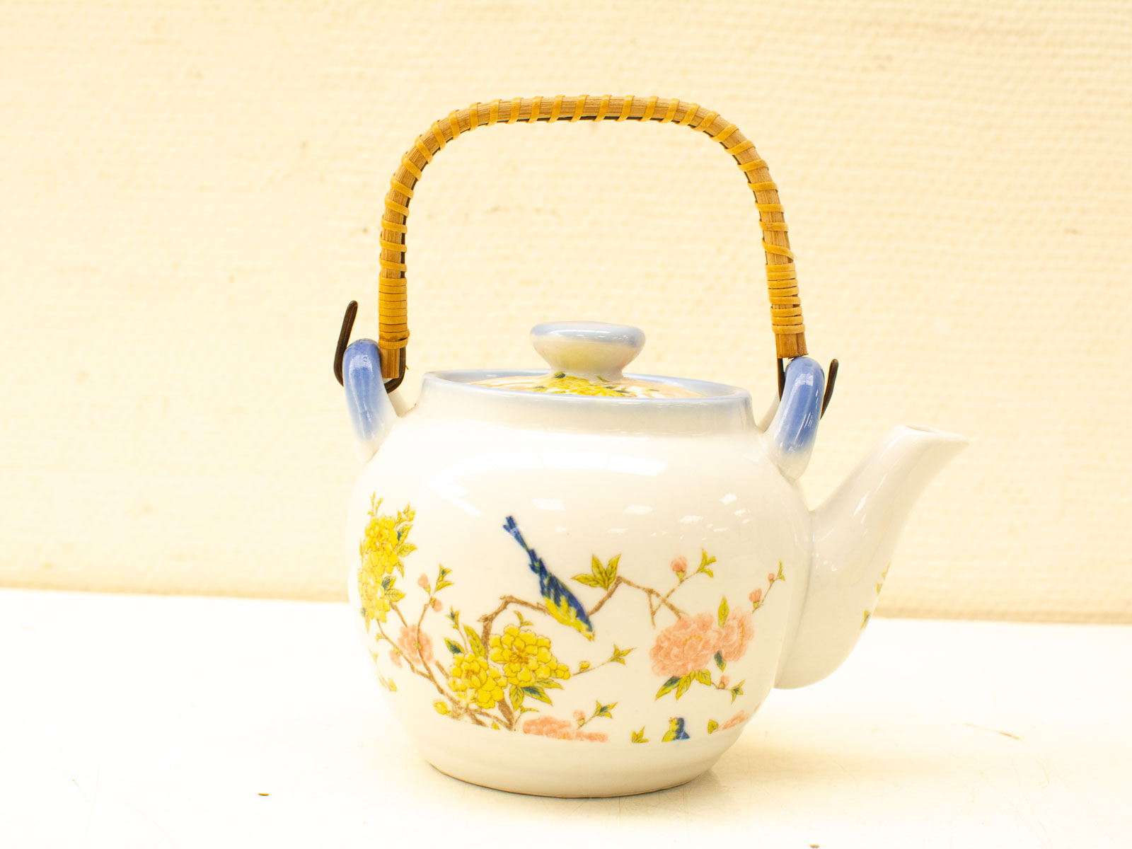 Charming porcelain teapot with vibrant floral design and woven handle for elegant tea serving.