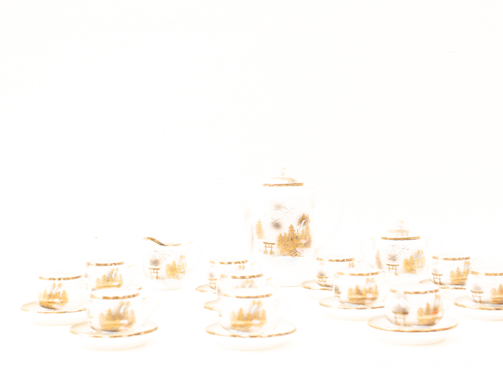 Elegant porcelain tea set with gold accents, featuring a teapot, creamer, and delicate cups.