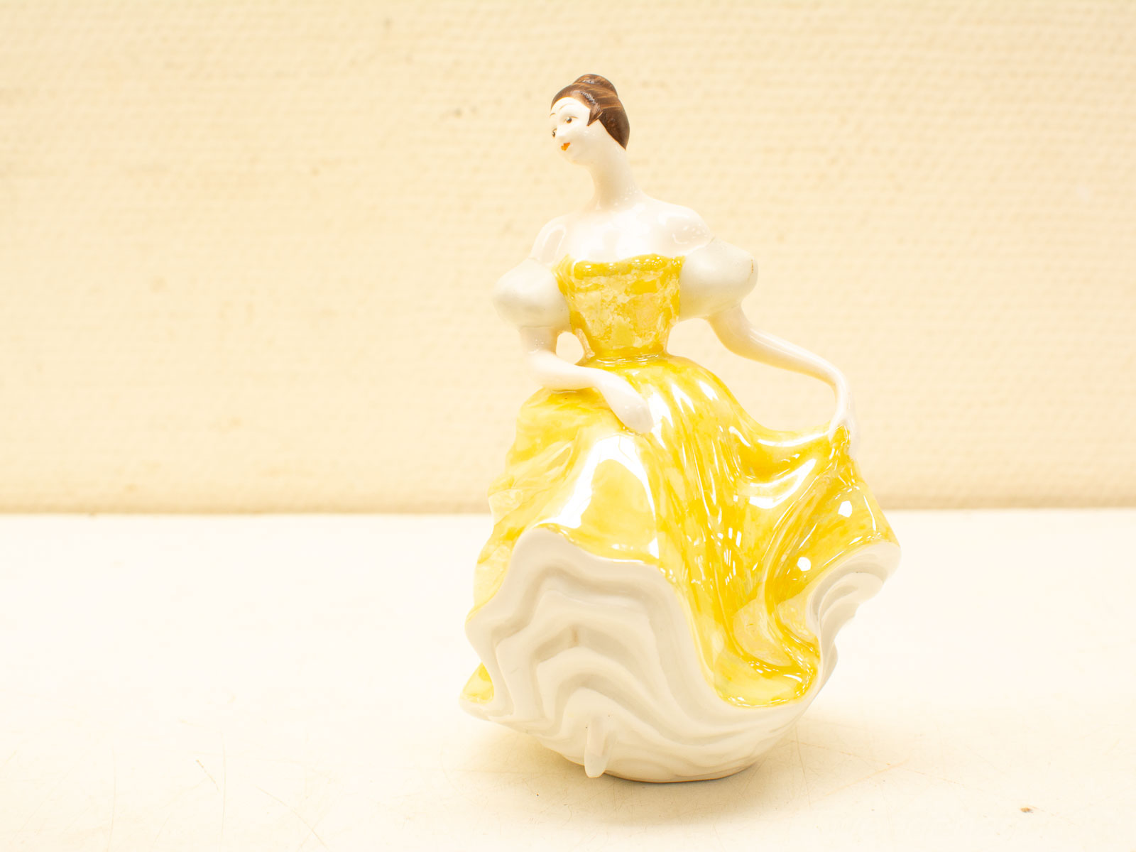 Elegant porcelain figurine of a woman in a vibrant yellow gown, showcasing exquisite craftsmanship.