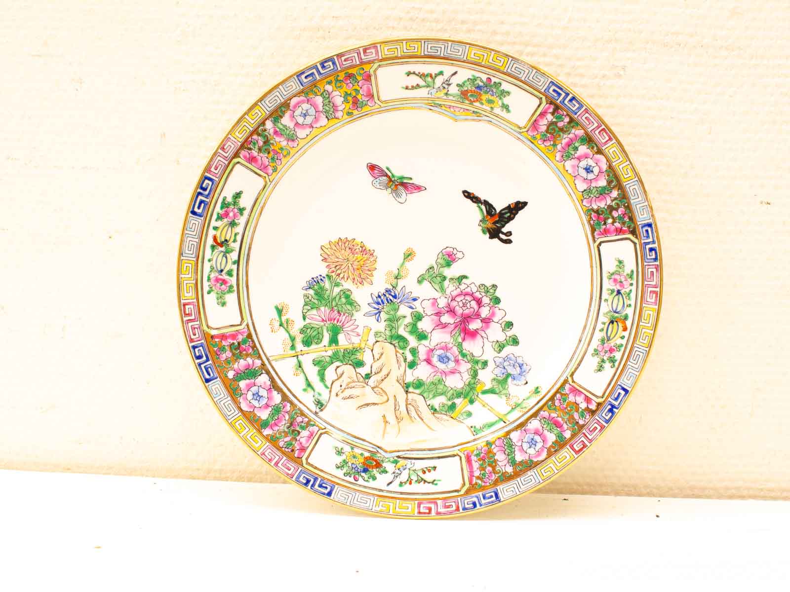 Vintage ceramic plate with vibrant floral design, butterflies, and intricate geometric border.