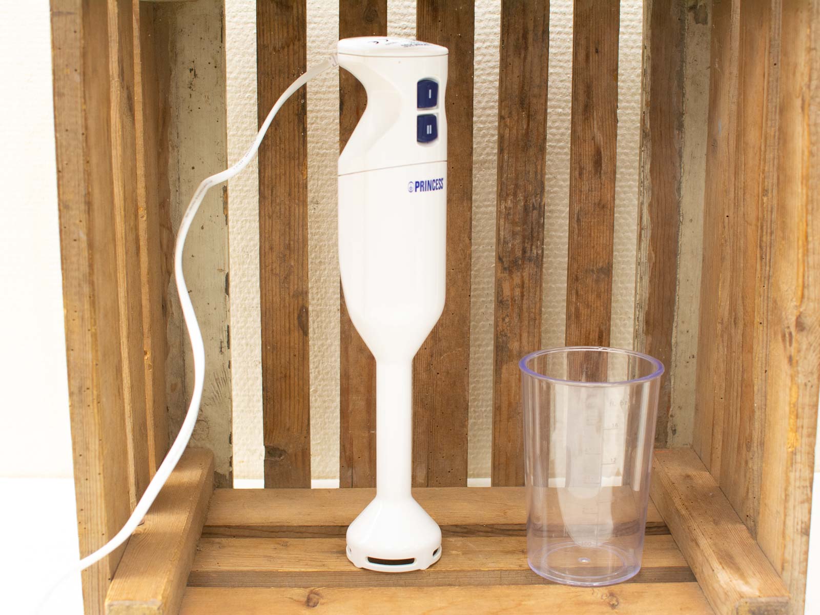 Sleek white hand blender and measuring cup on rustic wooden crate, perfect for any kitchen.