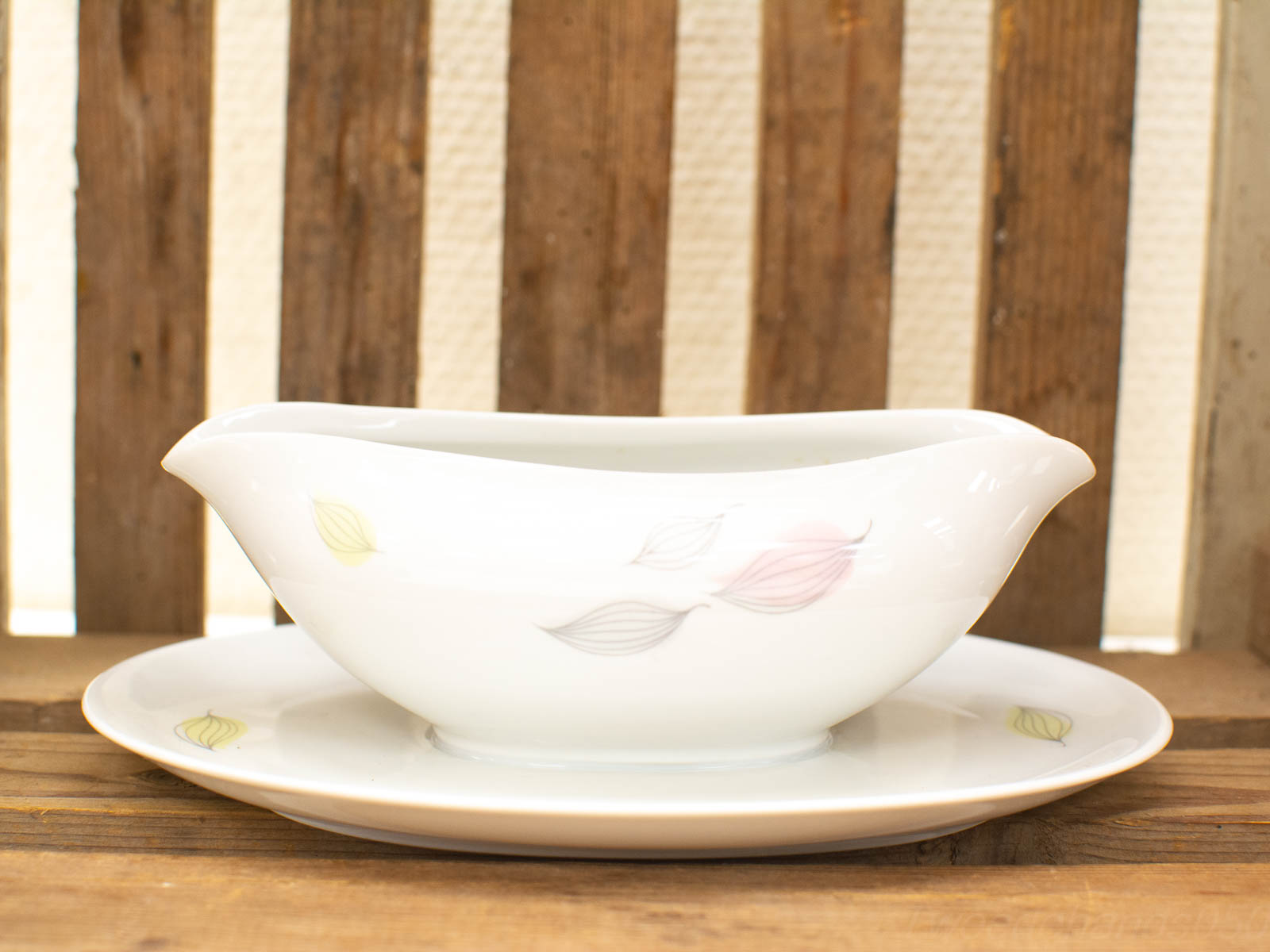 Elegant porcelain gravy boat with saucer featuring pastel leaves for refined dining experiences.