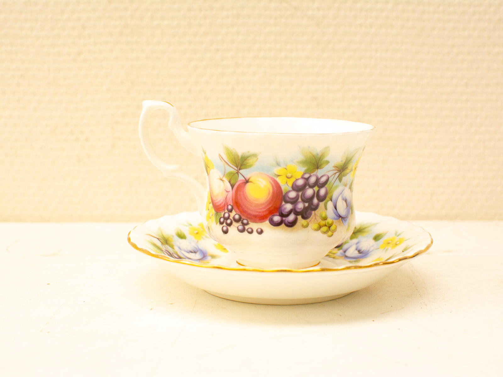 Vintage porcelain teacup and saucer with vibrant fruit design and elegant gold accents.