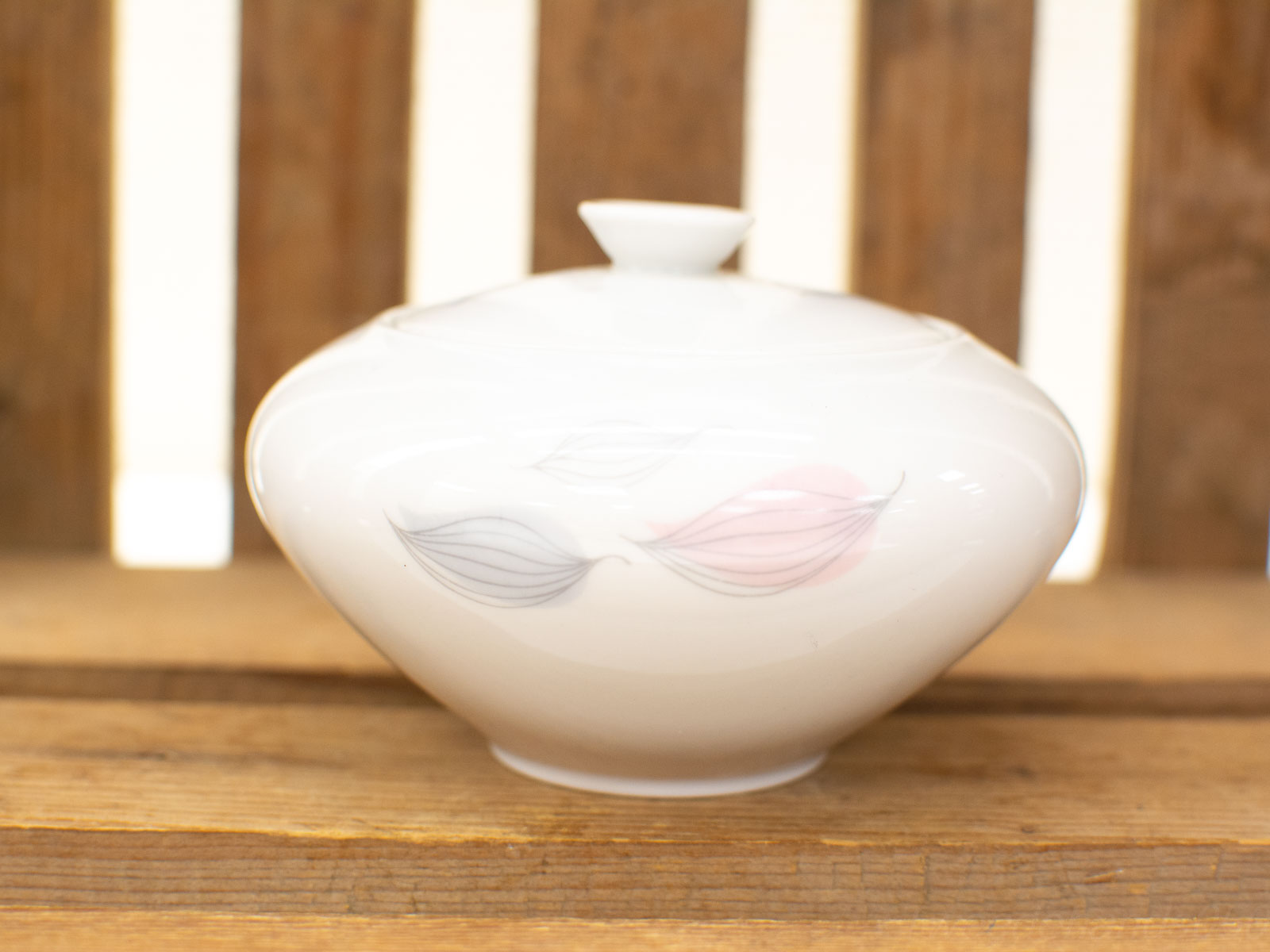 Elegant porcelain storage container with leaf motifs against a rustic wooden backdrop.