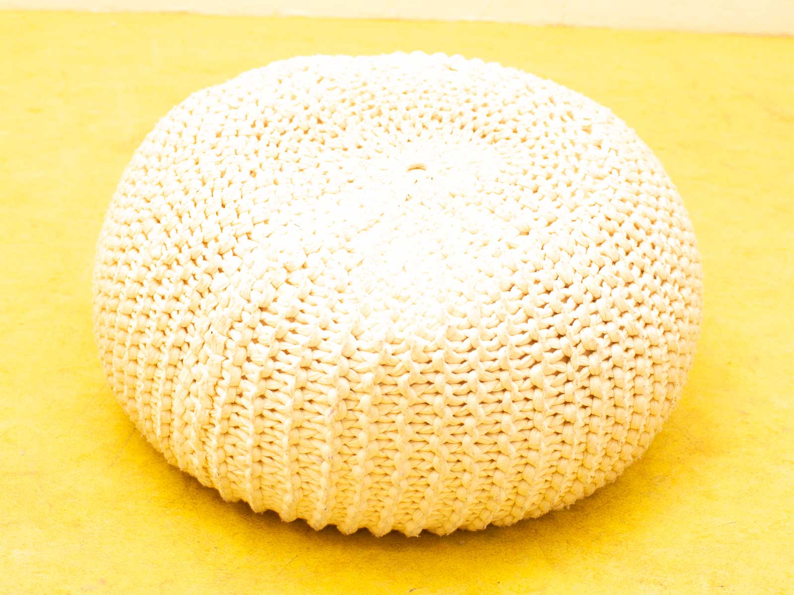 Cozy white pouf against bright yellow background, perfect for stylish home decor and seating.